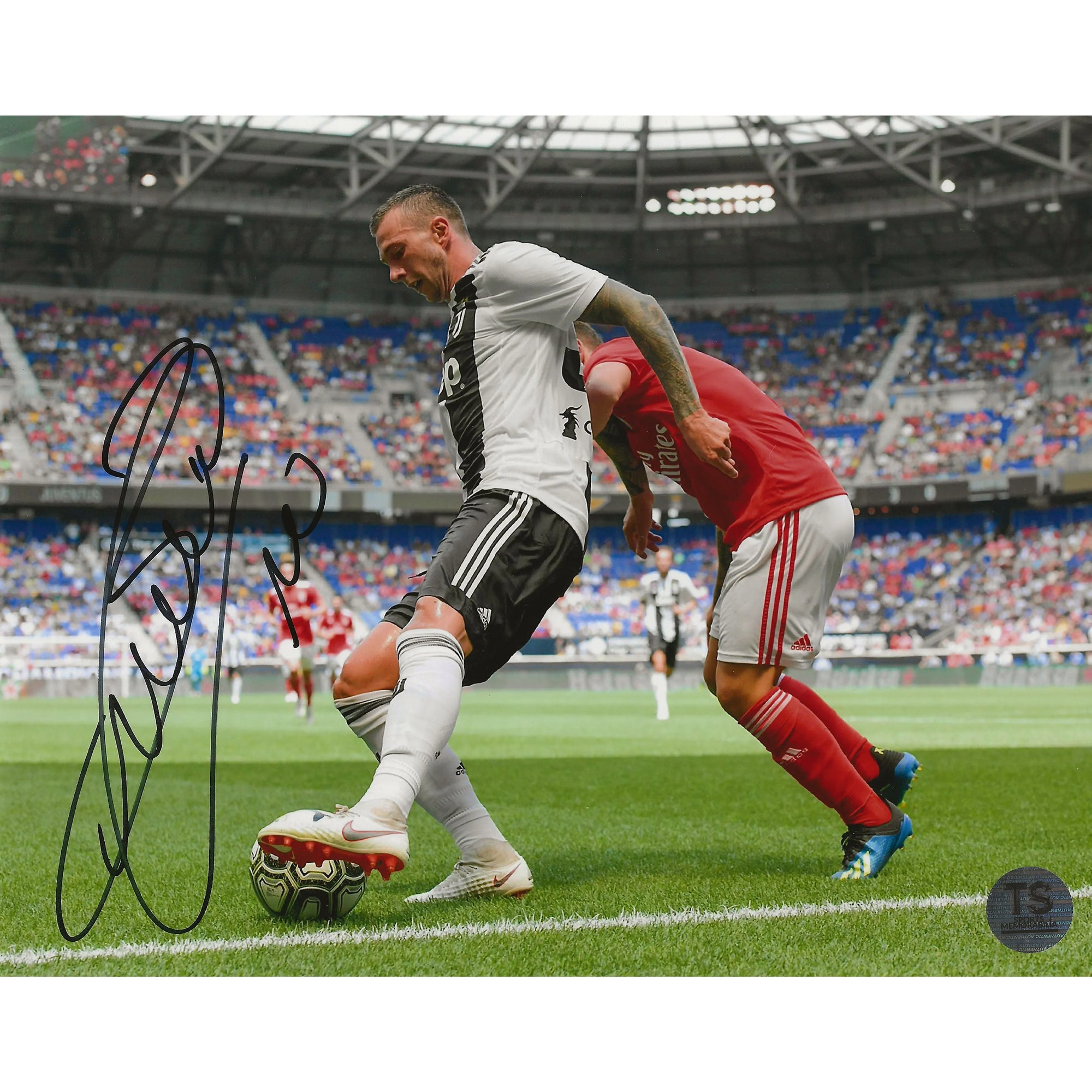 Soccer player in black and white jersey dribbling ball near sideline, stadium crowd, autograph
