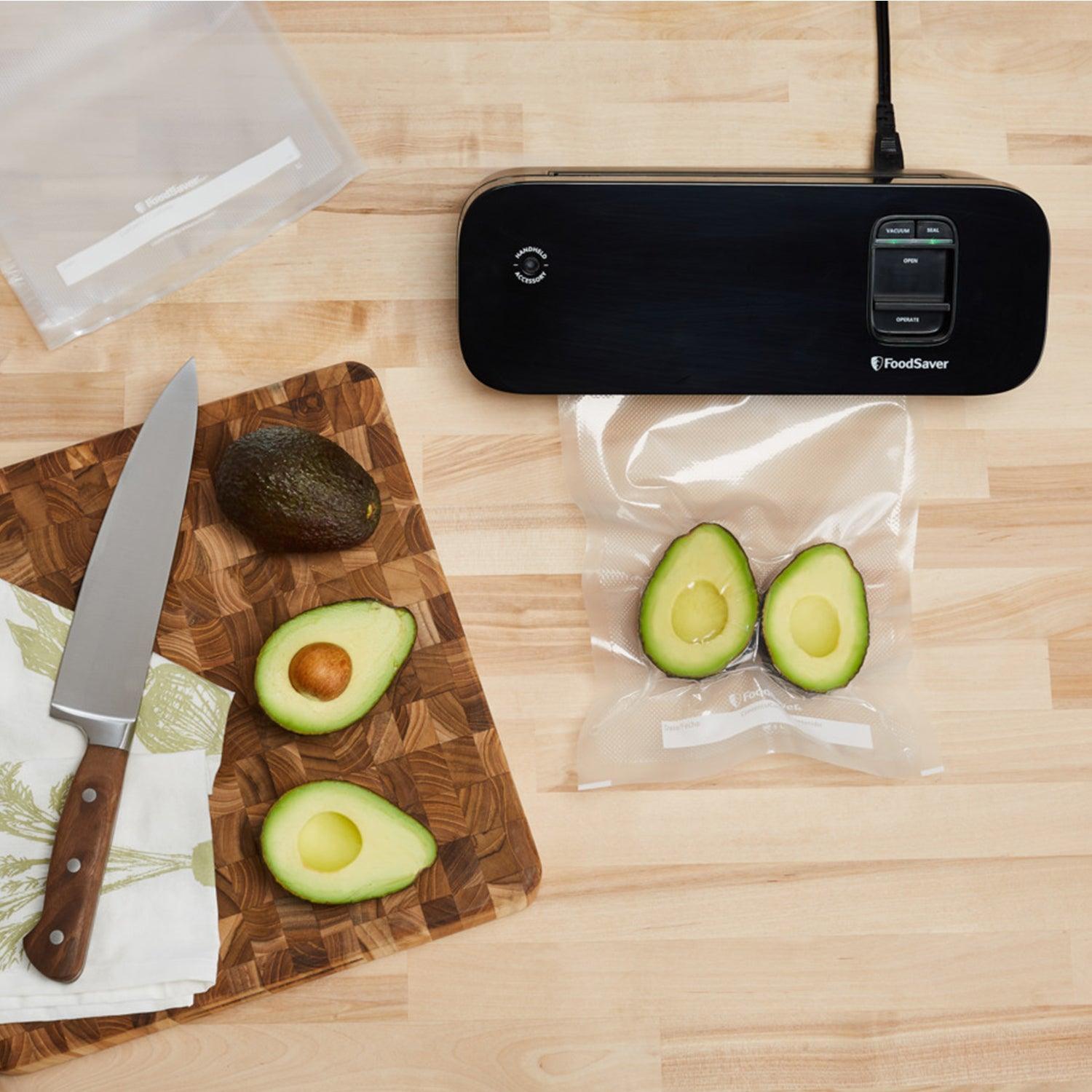 FoodSaver vacuum sealer with avocado halves in vacuum bag, knife and cutting board on counter