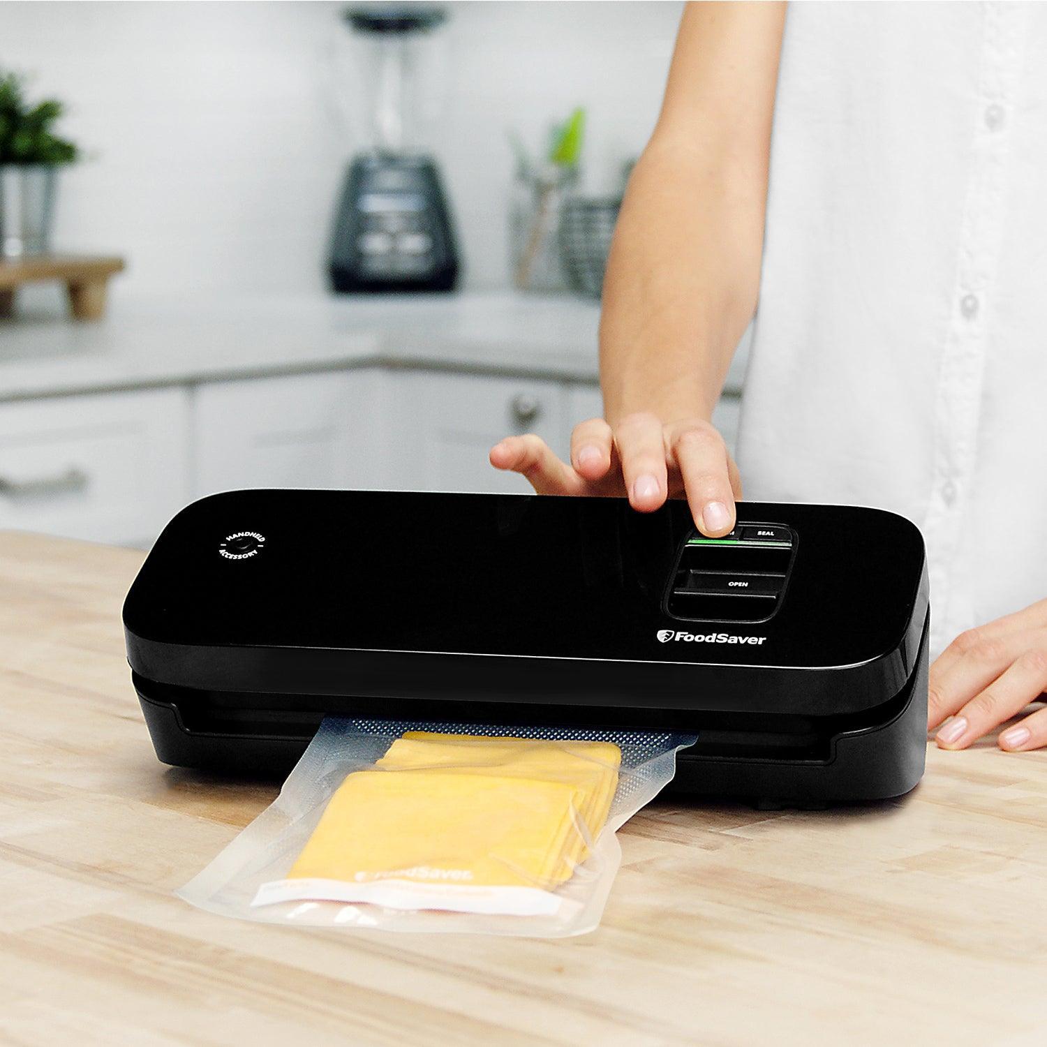 FoodSaver vacuum sealer sealing cheese in kitchen on wood countertop, person pressing button