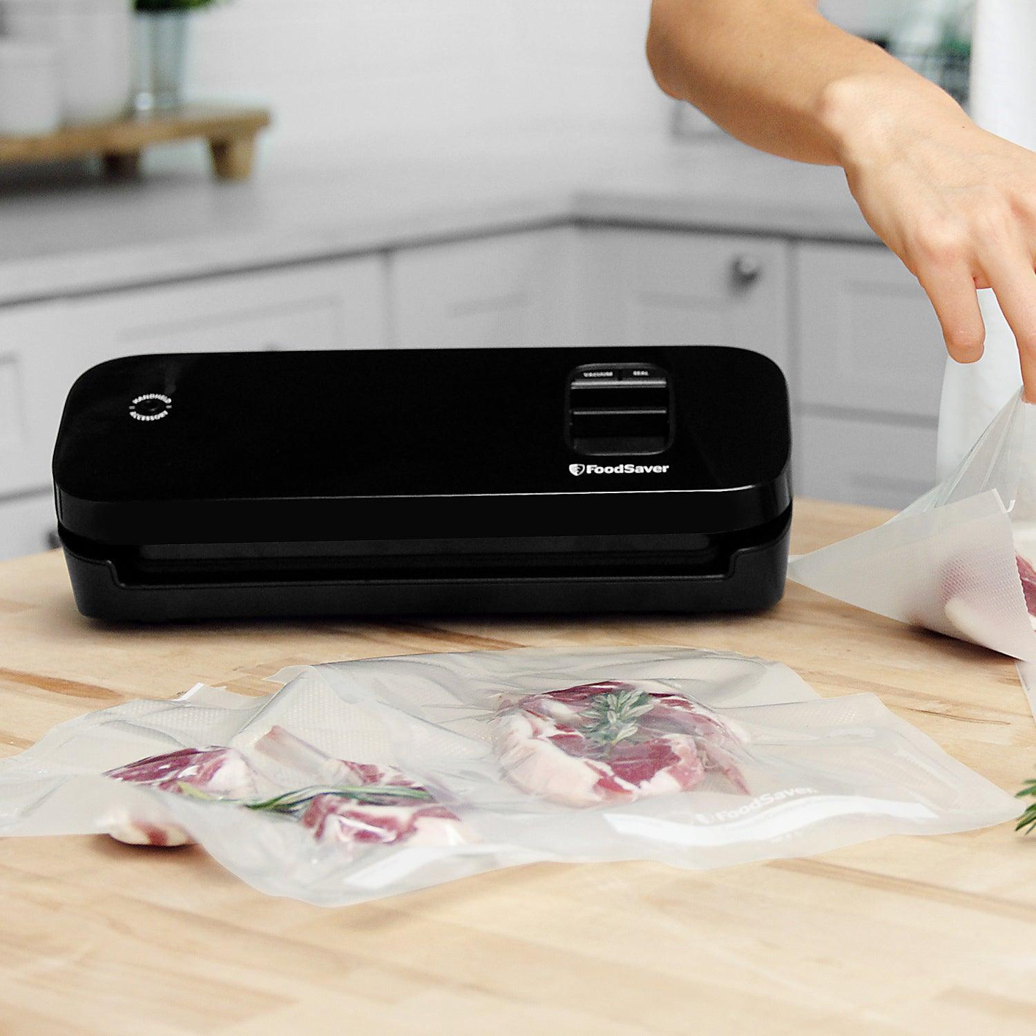 FoodSaver vacuum sealer in black sealing steak in vacuum bags on a kitchen countertop