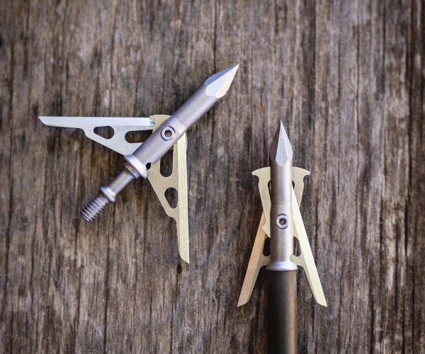 Two mechanical broadhead arrow tips on rustic wood background, hunting gear close-up