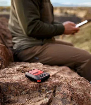 Man outdoors with portable GPS tracker device on rocky surface, remote hiking technology