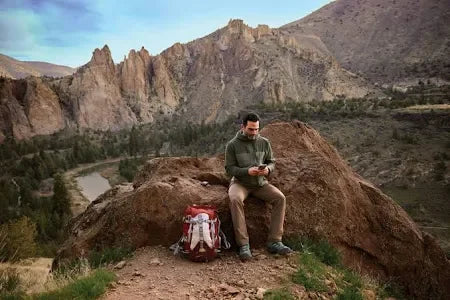Man sitting on rock with backpack in mountainous outdoor hiking setting
