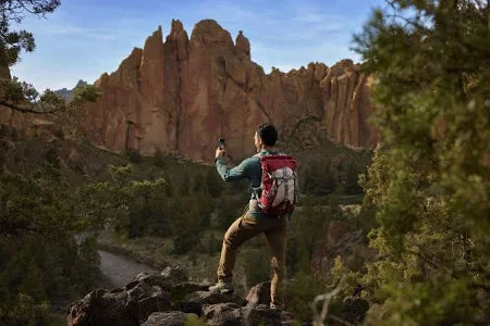Hiker with backpack taking photo of rocky mountain landscape and river in forest