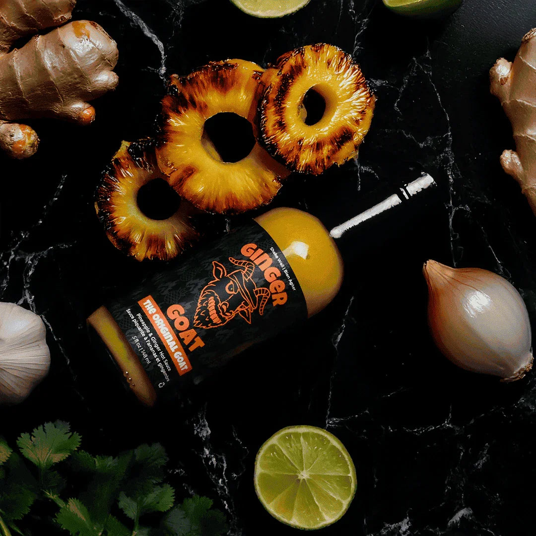Ginger Goat hot sauce bottle with grilled pineapple, ginger, lime, onion, garlic, and cilantro on black marble