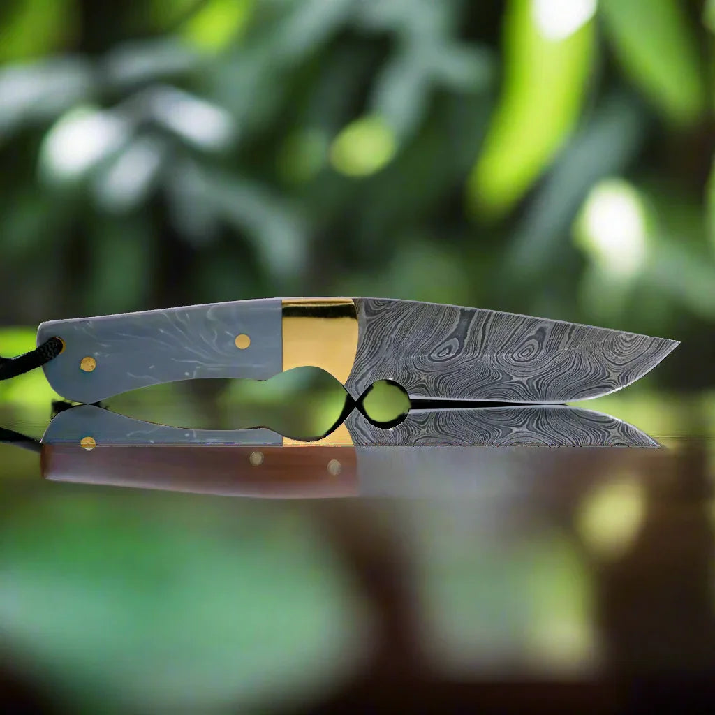 Damascus steel hunting knife with ornate blade and gray handle on wood, outdoors