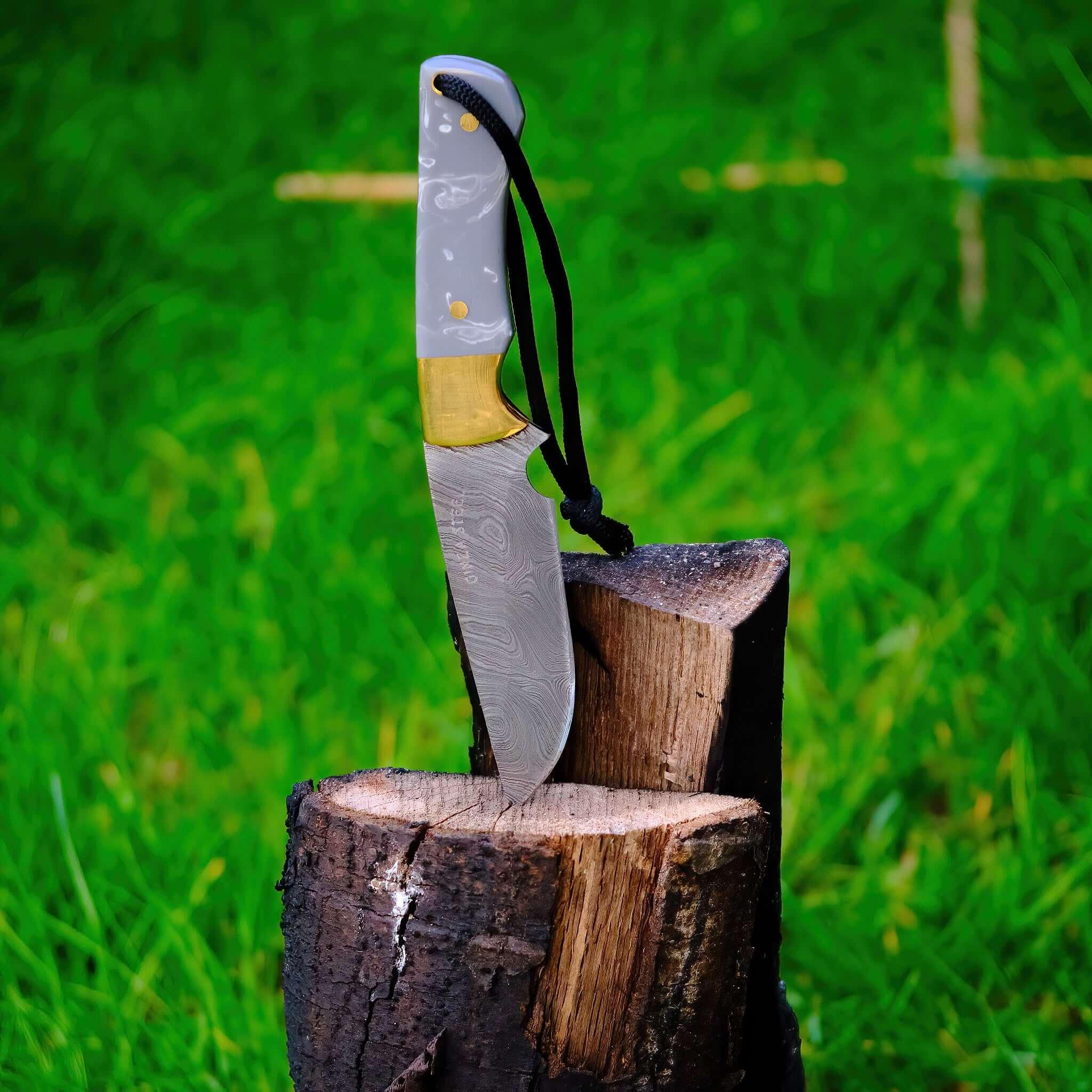 Damascus hunting knife with brass bolster in wood stump outdoors on green grass background