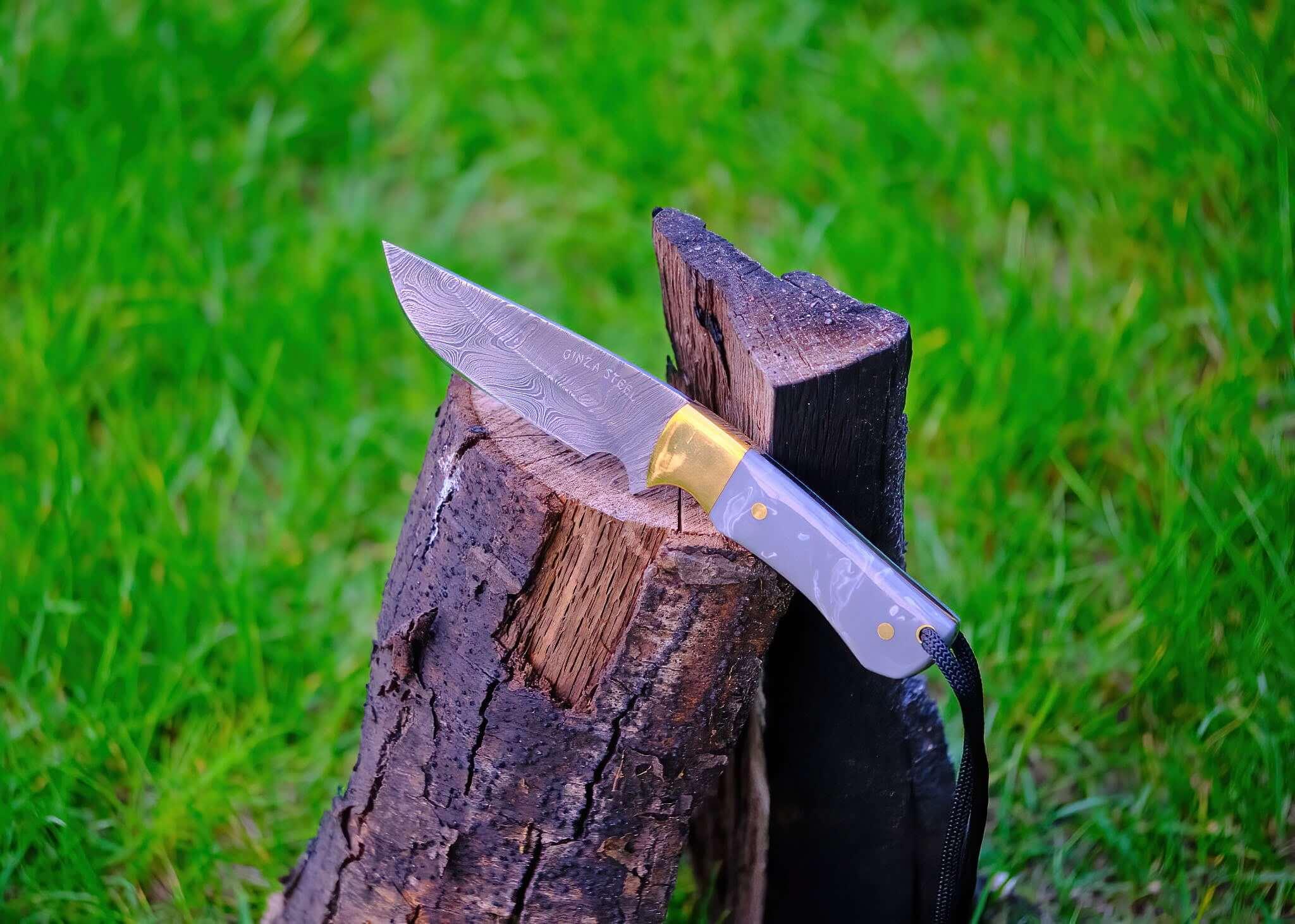 Damascus steel outdoor knife stuck in split log on green grass