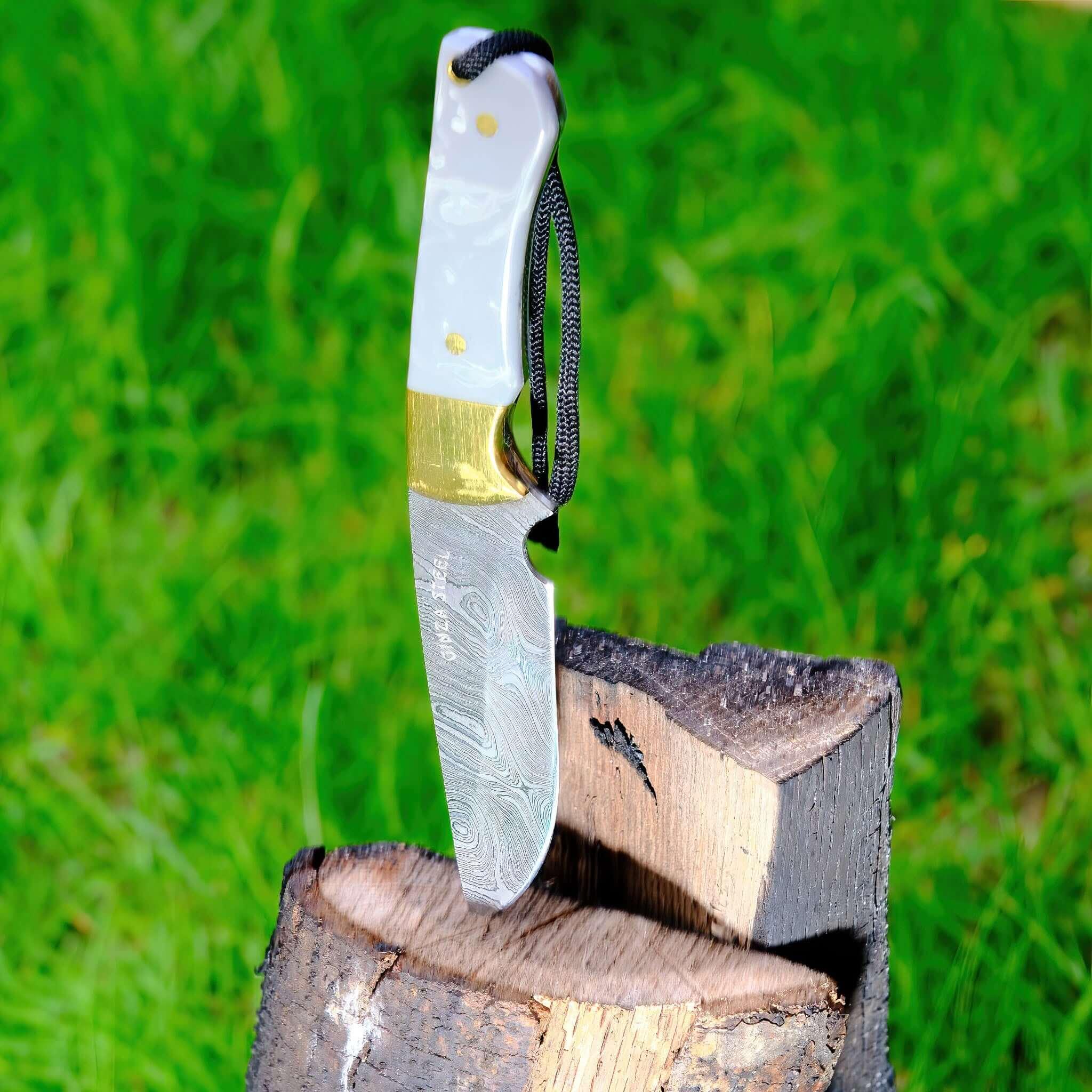 Damascus steel knife with white handle embedded in firewood outdoors on green grass