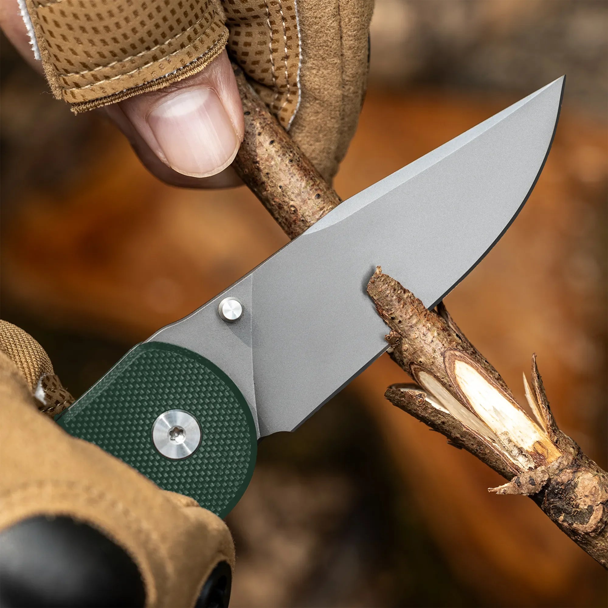Gloved hand using folding pocket knife to whittle a stick outdoors