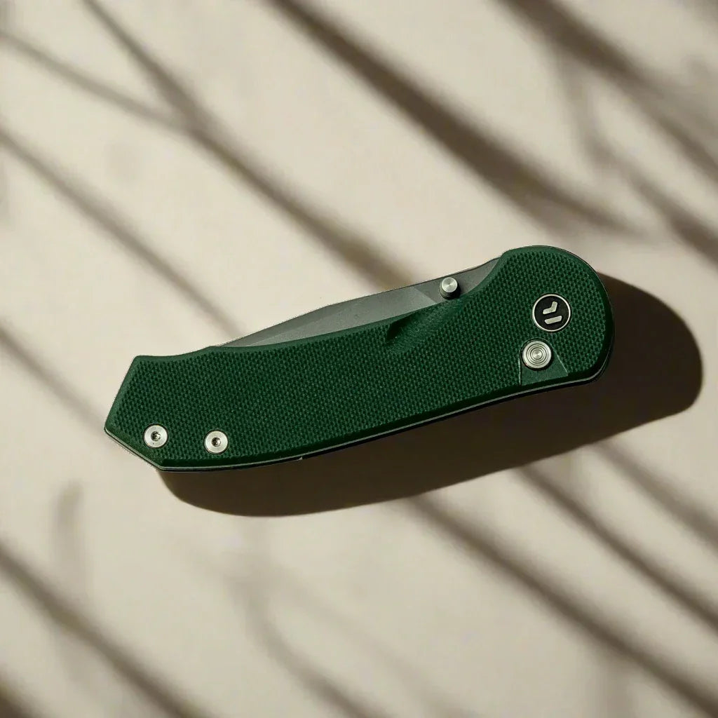 Green textured folding pocket knife on beige surface with soft shadows