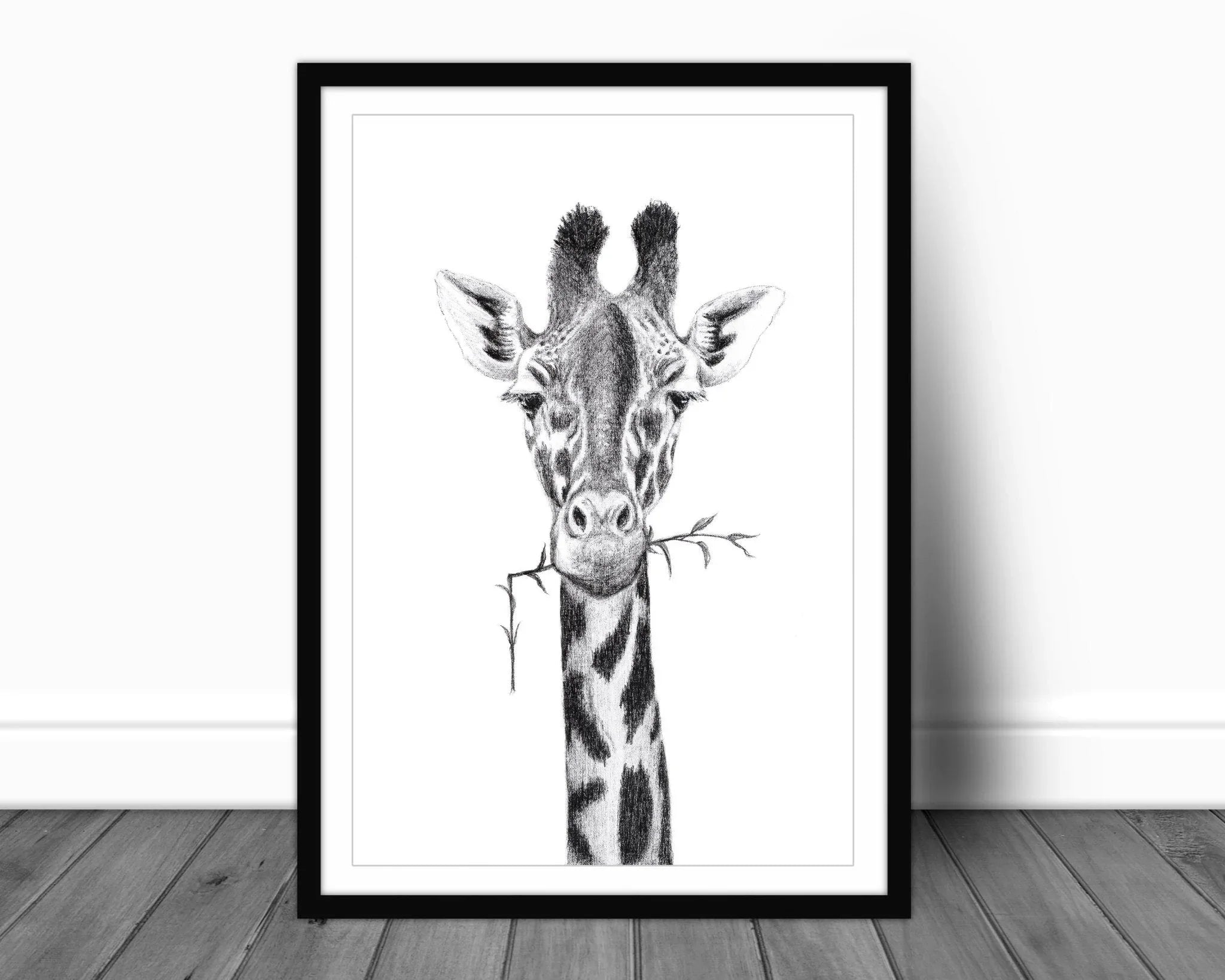 Framed black and white giraffe portrait drawing with branch, art print on wooden floor