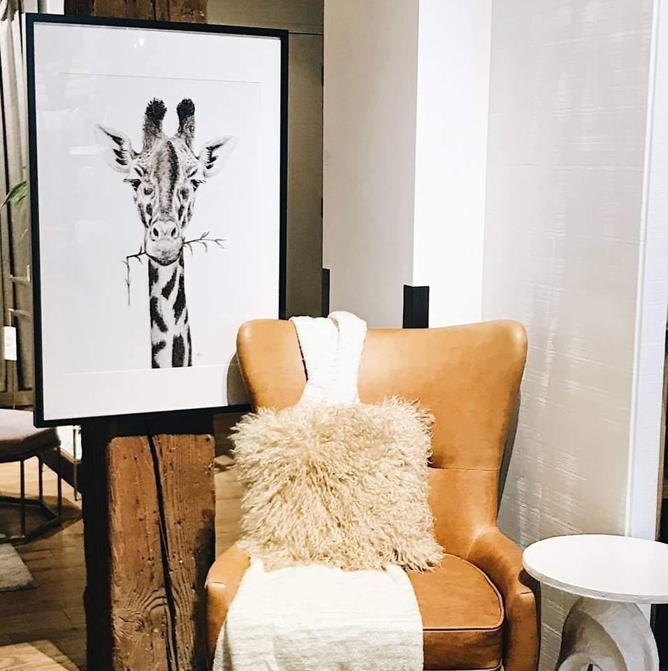 Framed giraffe portrait art in a modern living room with tan leather chair and fluffy pillow