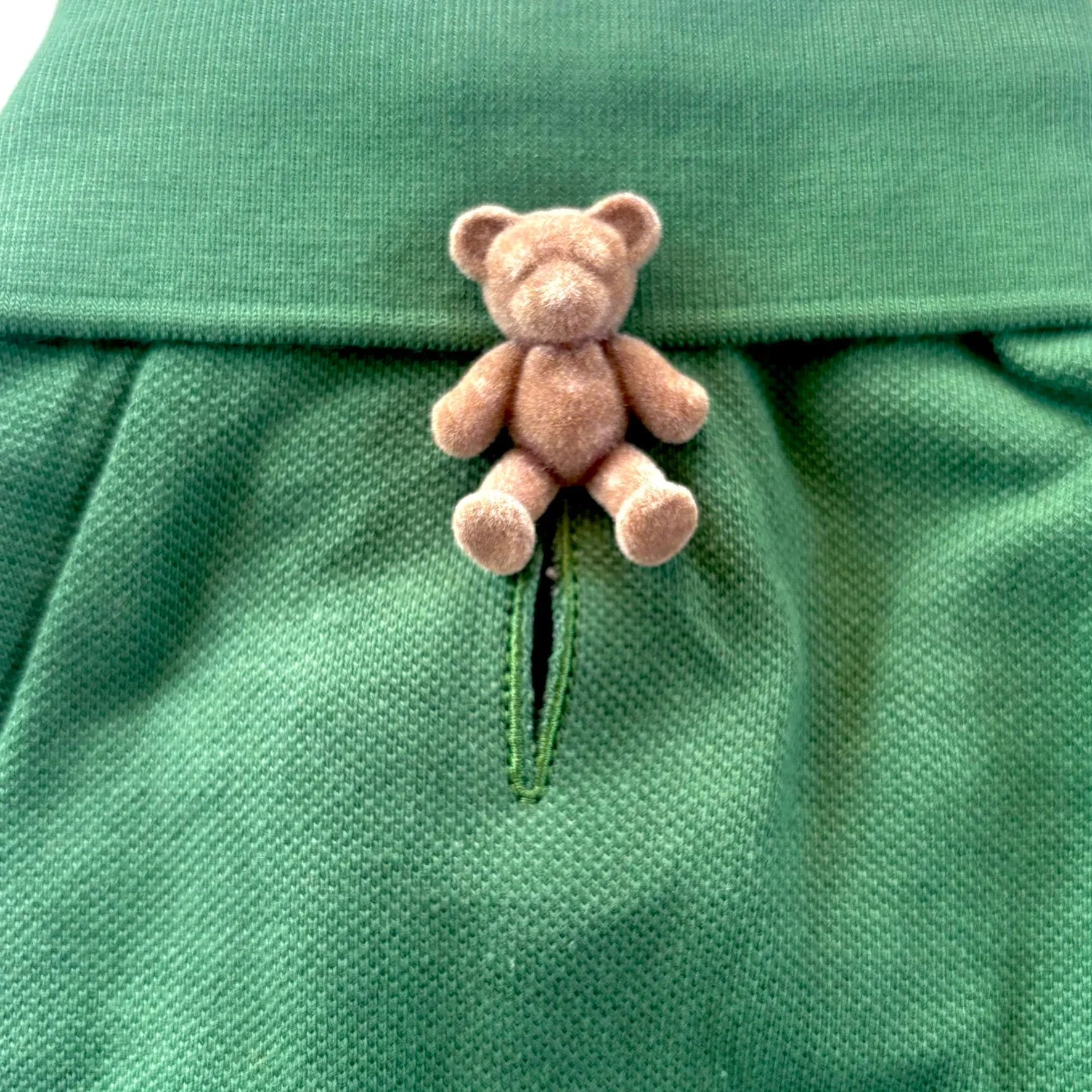 Small plush bear on green textured fabric skirt with waistband detail