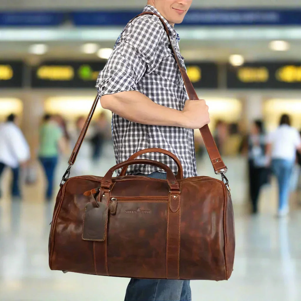 Man in plaid shirt carrying brown leather duffel bag with shoulder strap at airport
