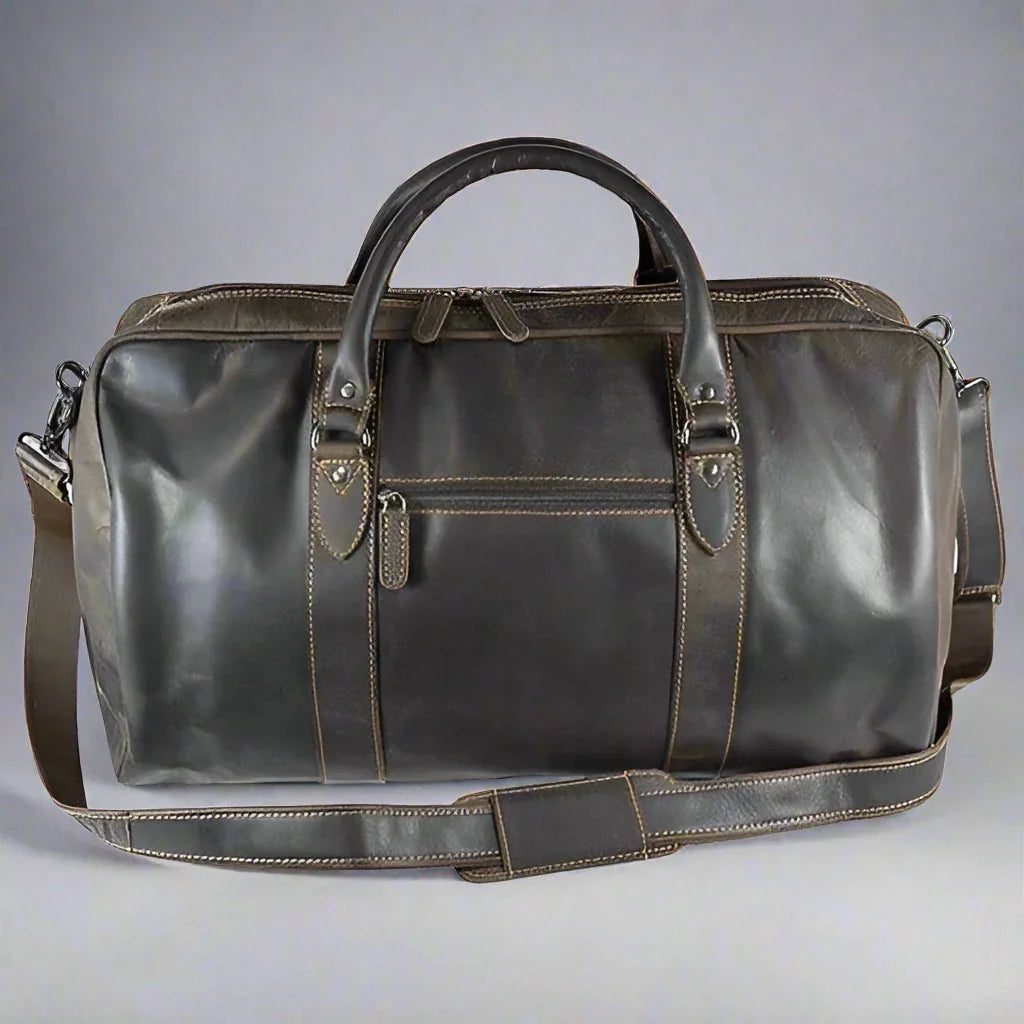 Brown leather travel bag with shoulder strap and front zipper pocket on gray background