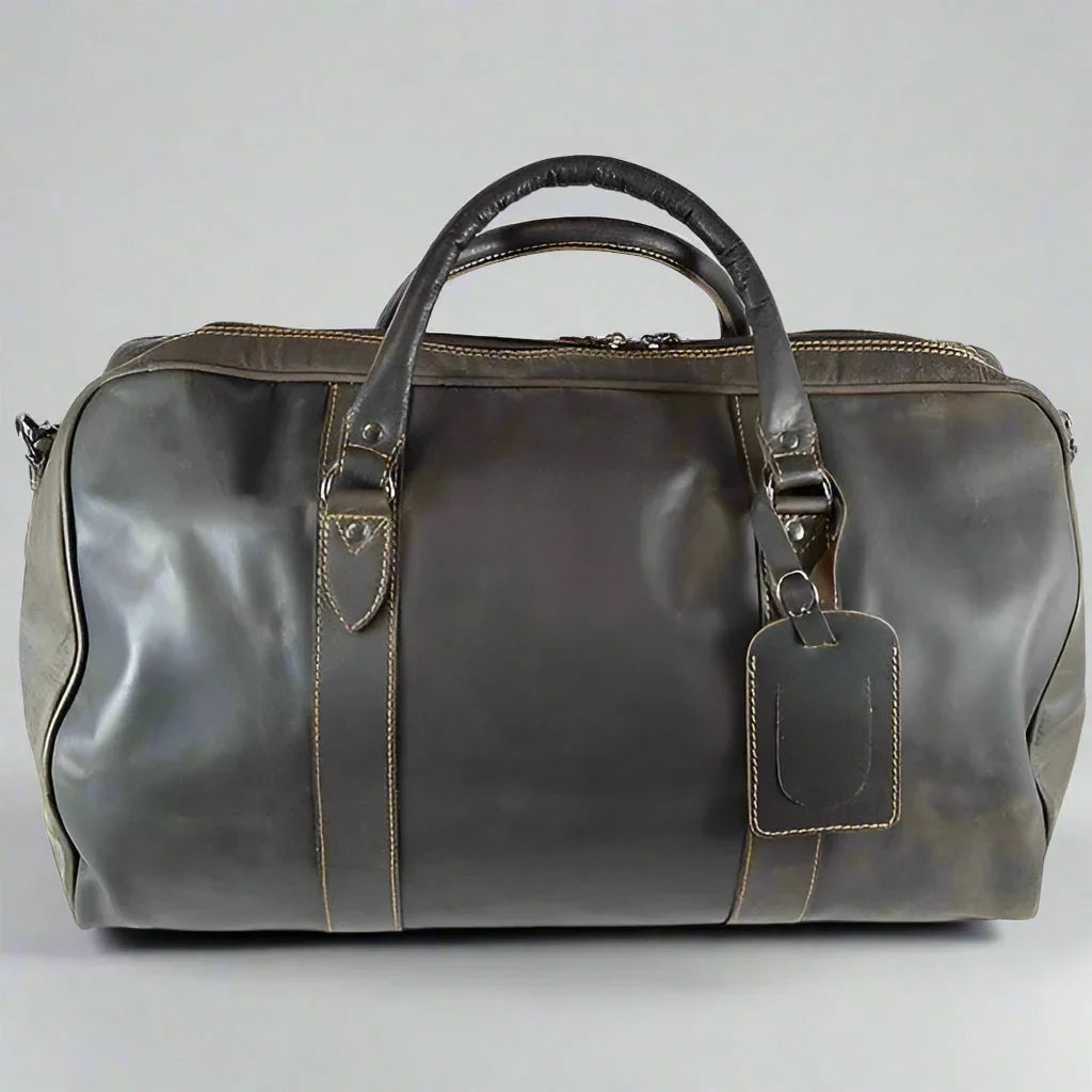 Brown leather travel bag with handles and luggage tag on a plain background