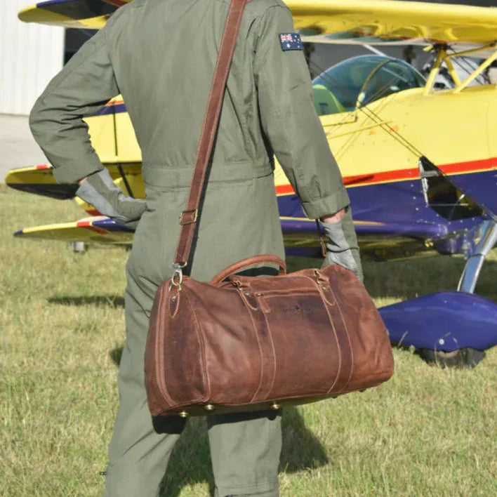 Brown leather travel bag on pilot in green suit, yellow biplane in background