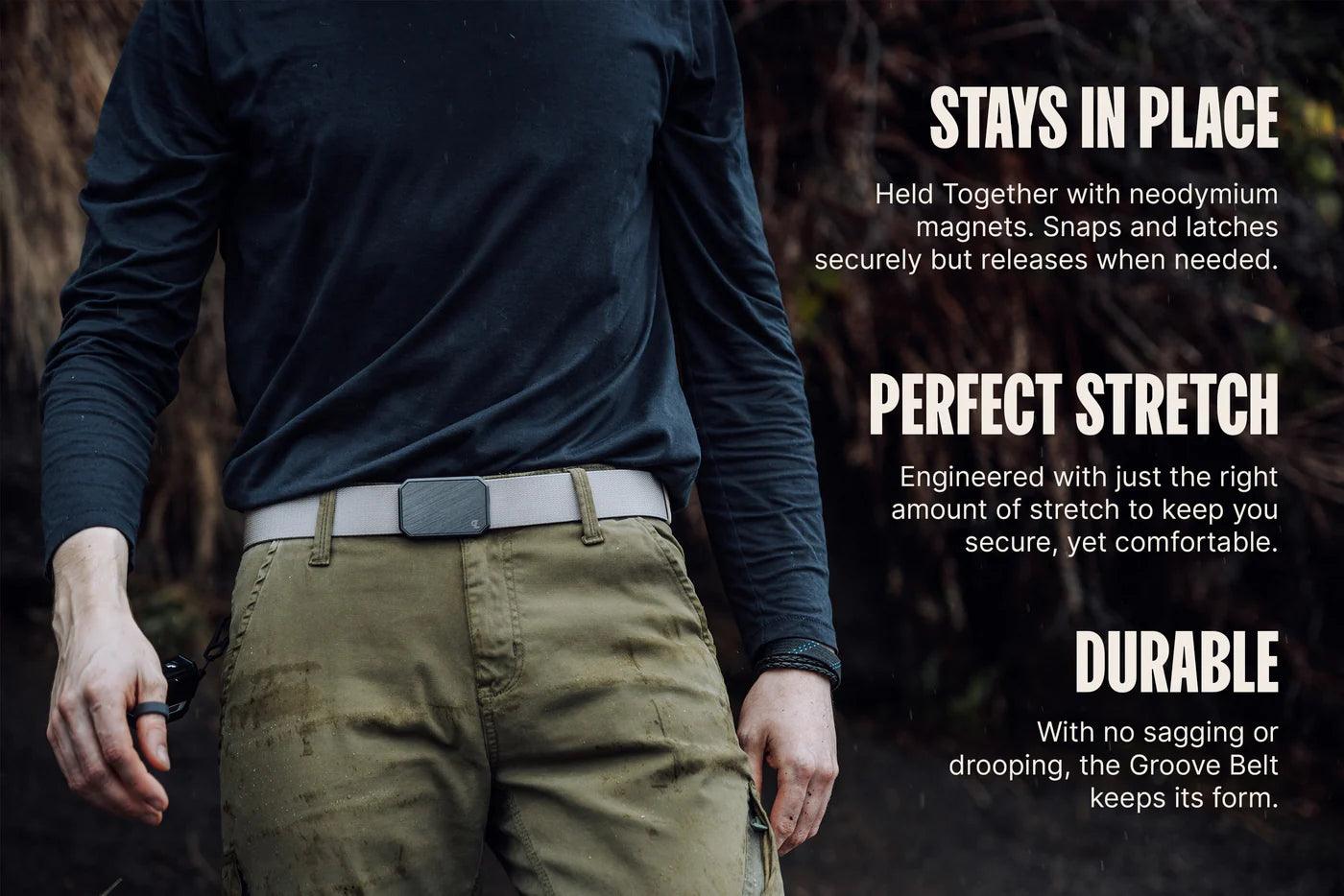 Man wearing khaki pants and a light gray tactical belt with text highlighting belt’s durability, stretch, and secure fit.