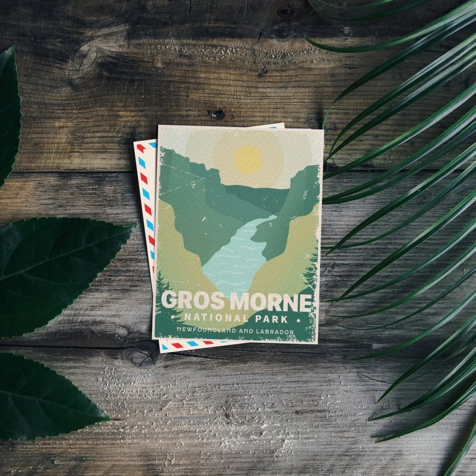 Gros Morne National Park postcard on wood table with green leaves, Newfoundland and Labrador