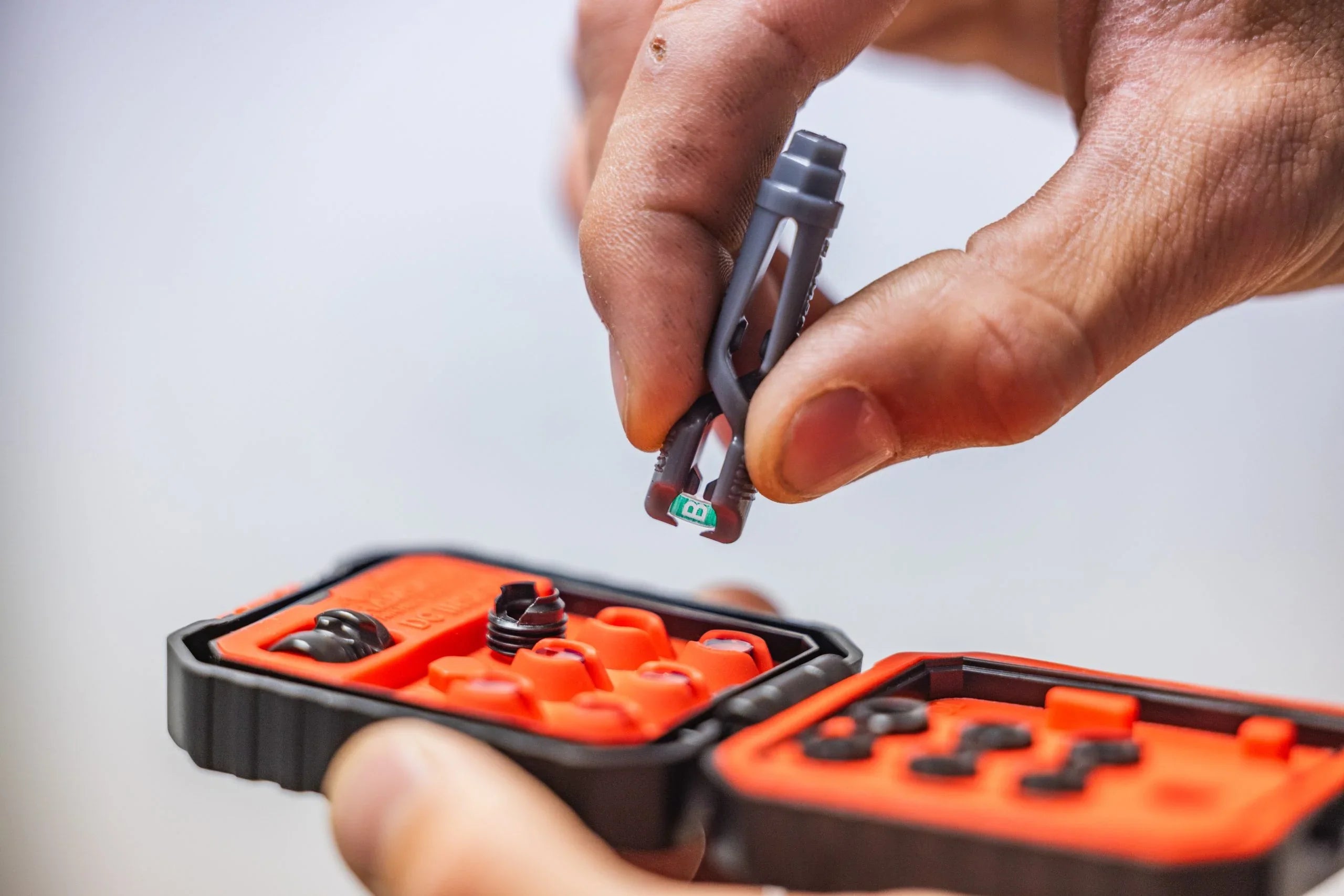 Hand holding tool above orange bike tubeless tire repair kit