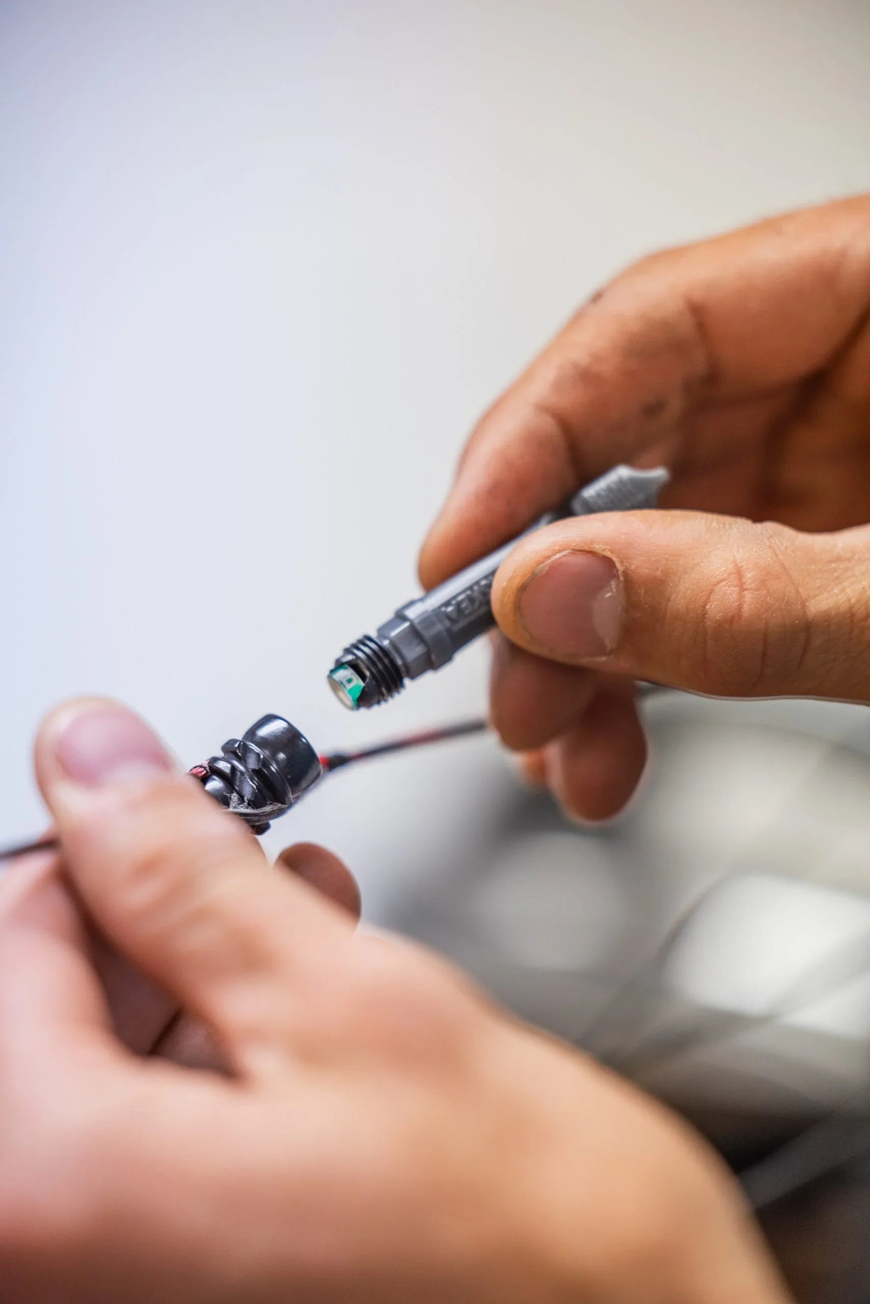 Hands assembling electrical connector with exposed wiring, close up, workshop setting