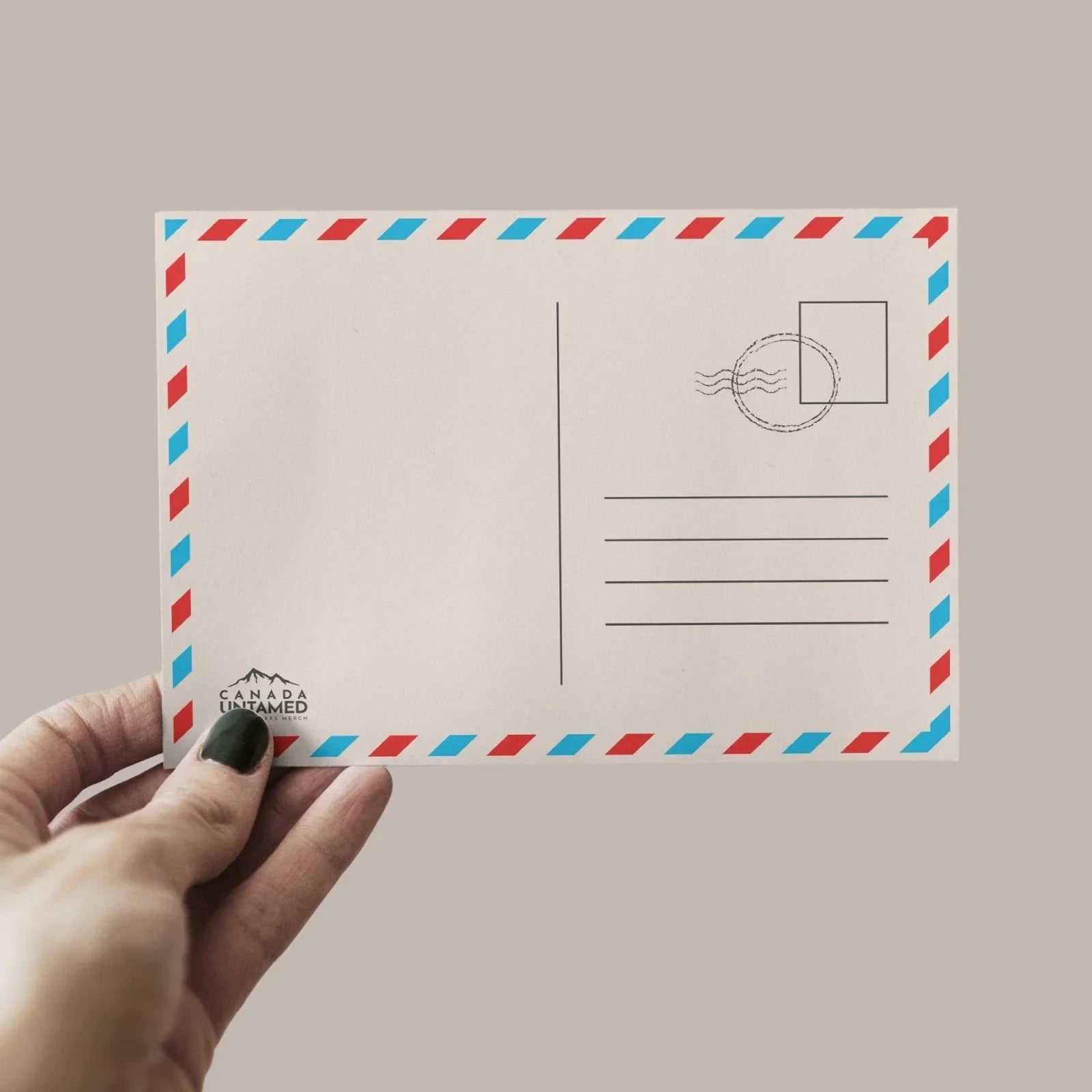 Hand holding blank postcard with red and blue border, Canada Untamed logo, plain background