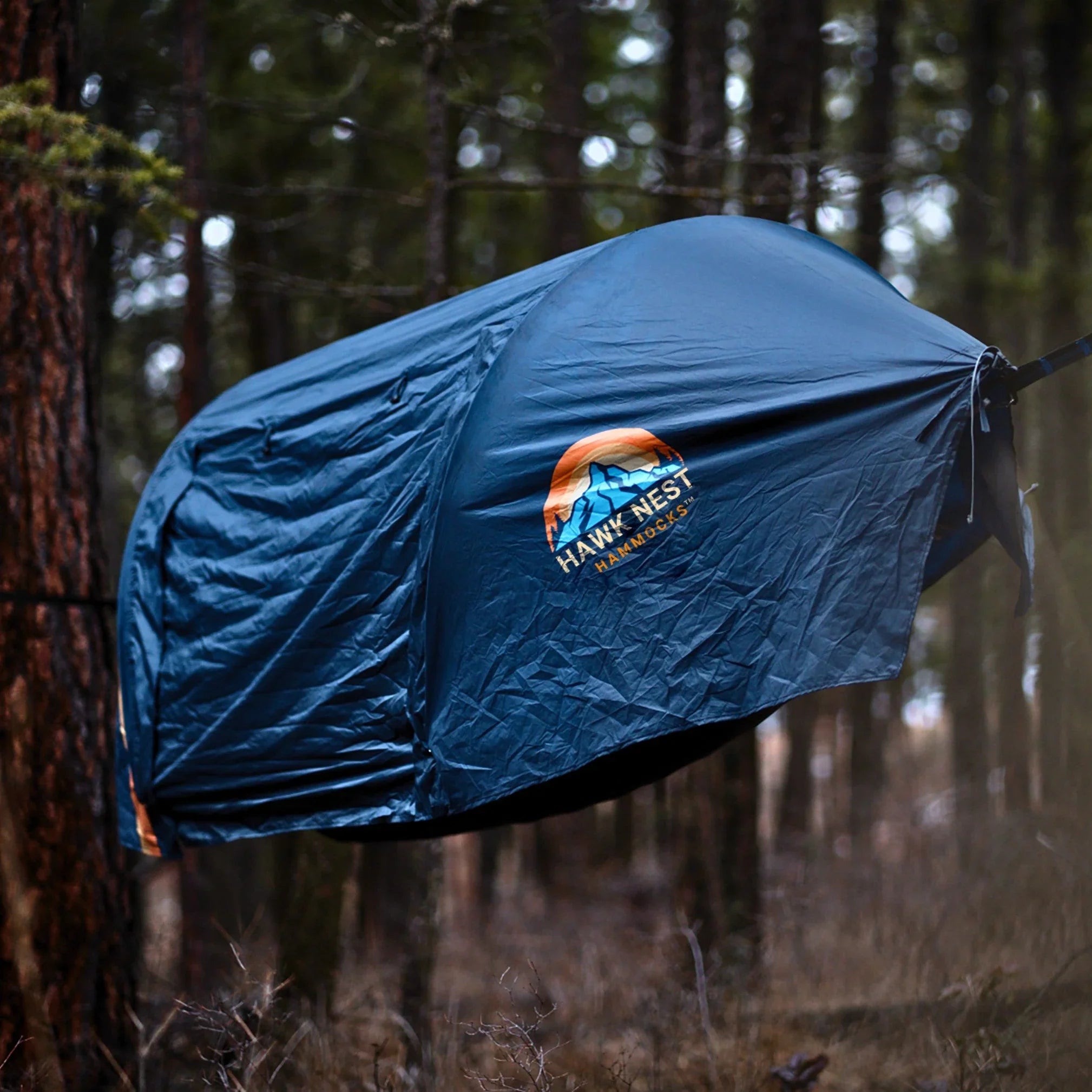 Blue Hawk Nest Hammocks tent hanging between trees in a forest