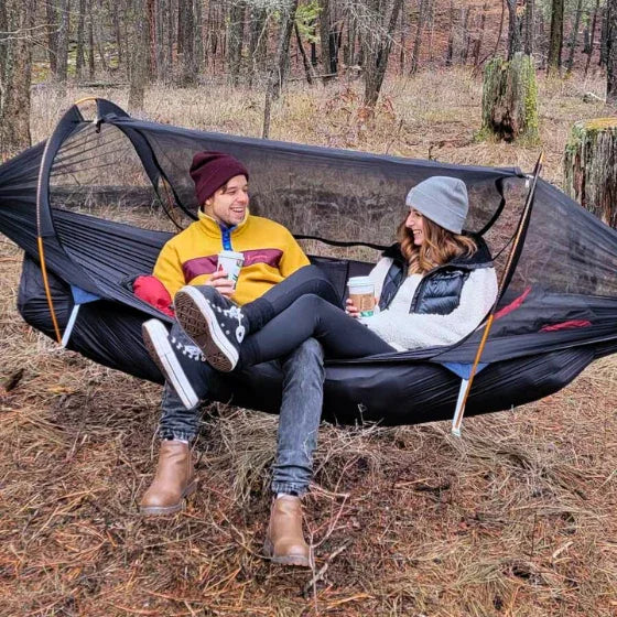 Couple relaxing in outdoor camping hammock with bug net, forest setting