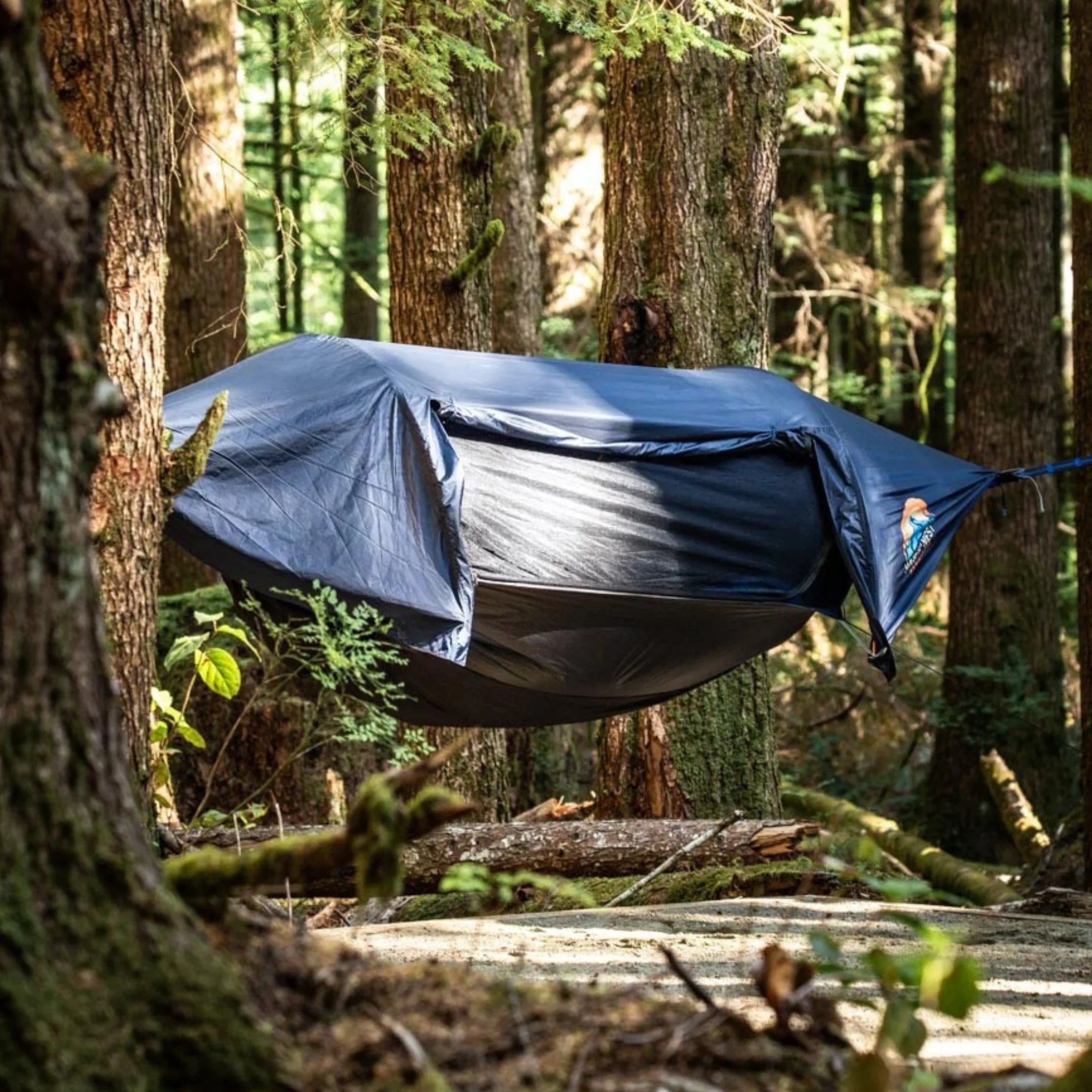 Camping hammock tent with rainfly suspended between trees in a forest