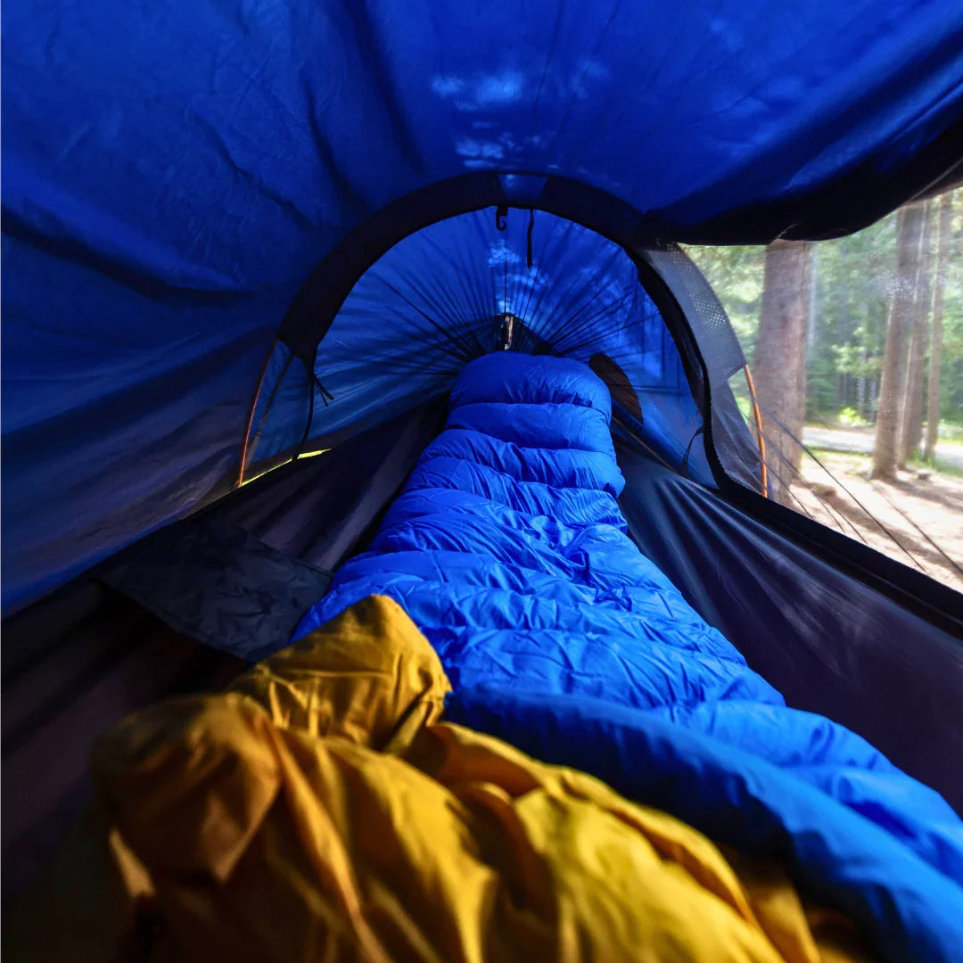 Blue sleeping bag inside a small camping tent in a forest setting