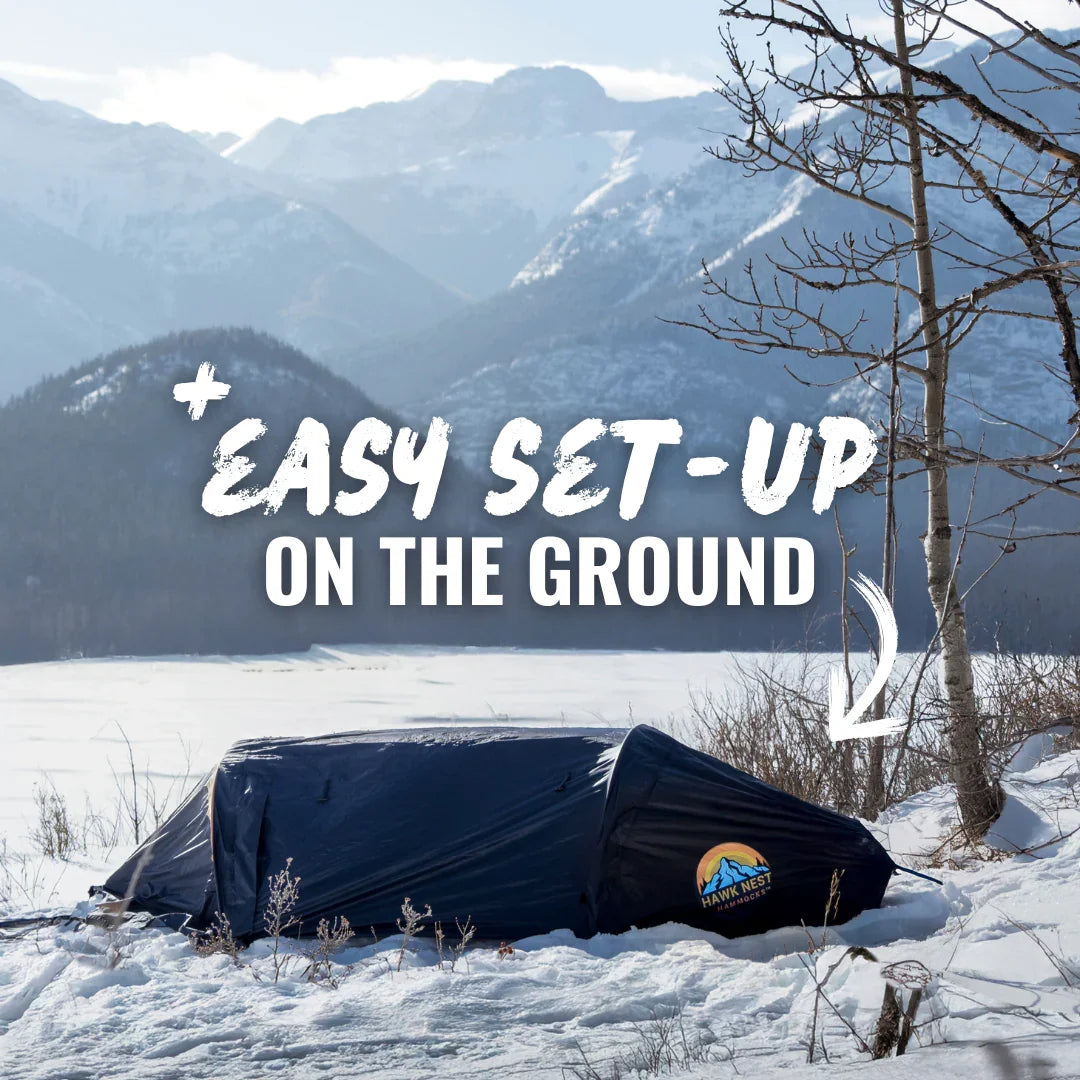 Winter camping tent pitched on snow with mountains in background, Hawk Nest Outdoors logo visible.