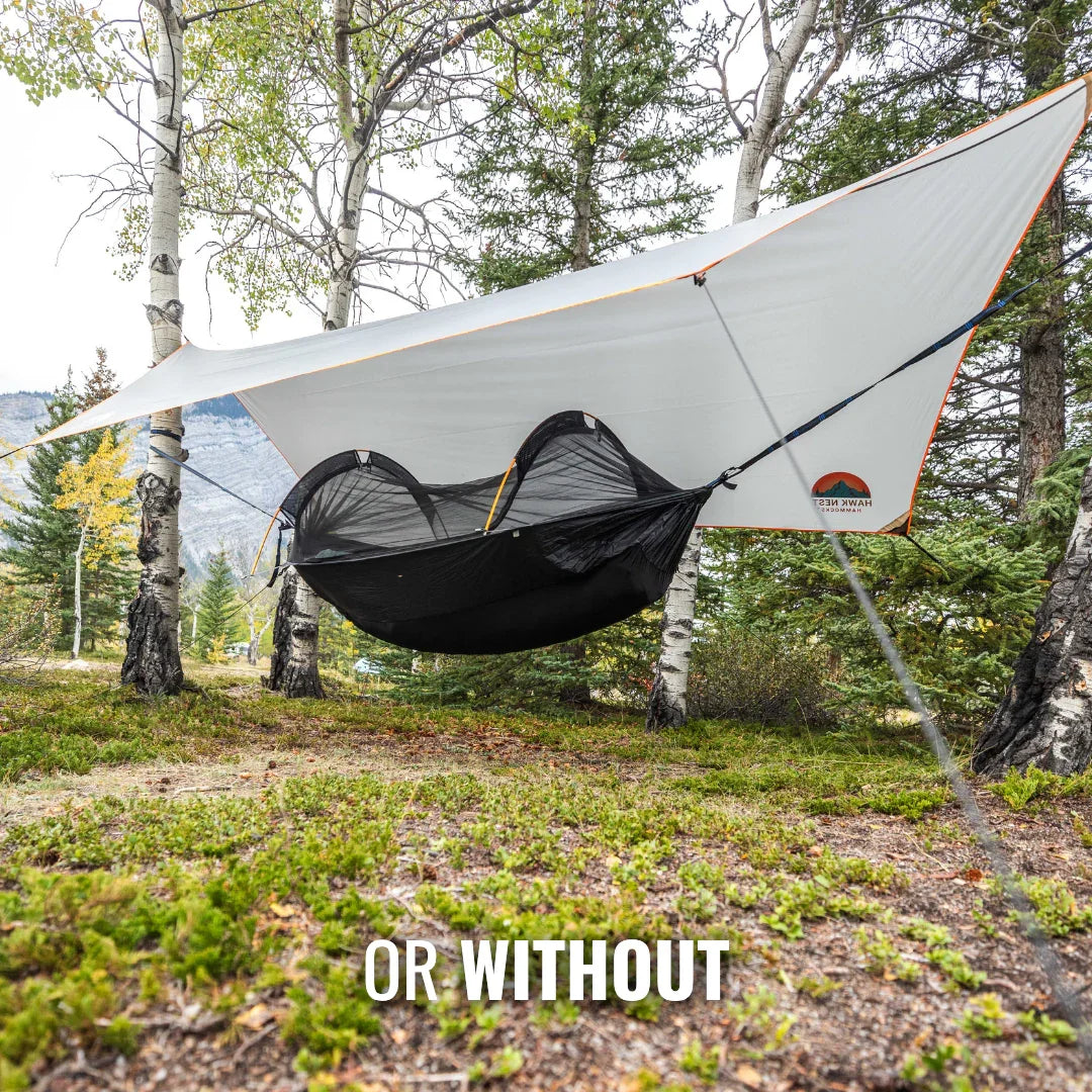 Camping hammock with bug net and rain tarp setup between trees in forest outdoors