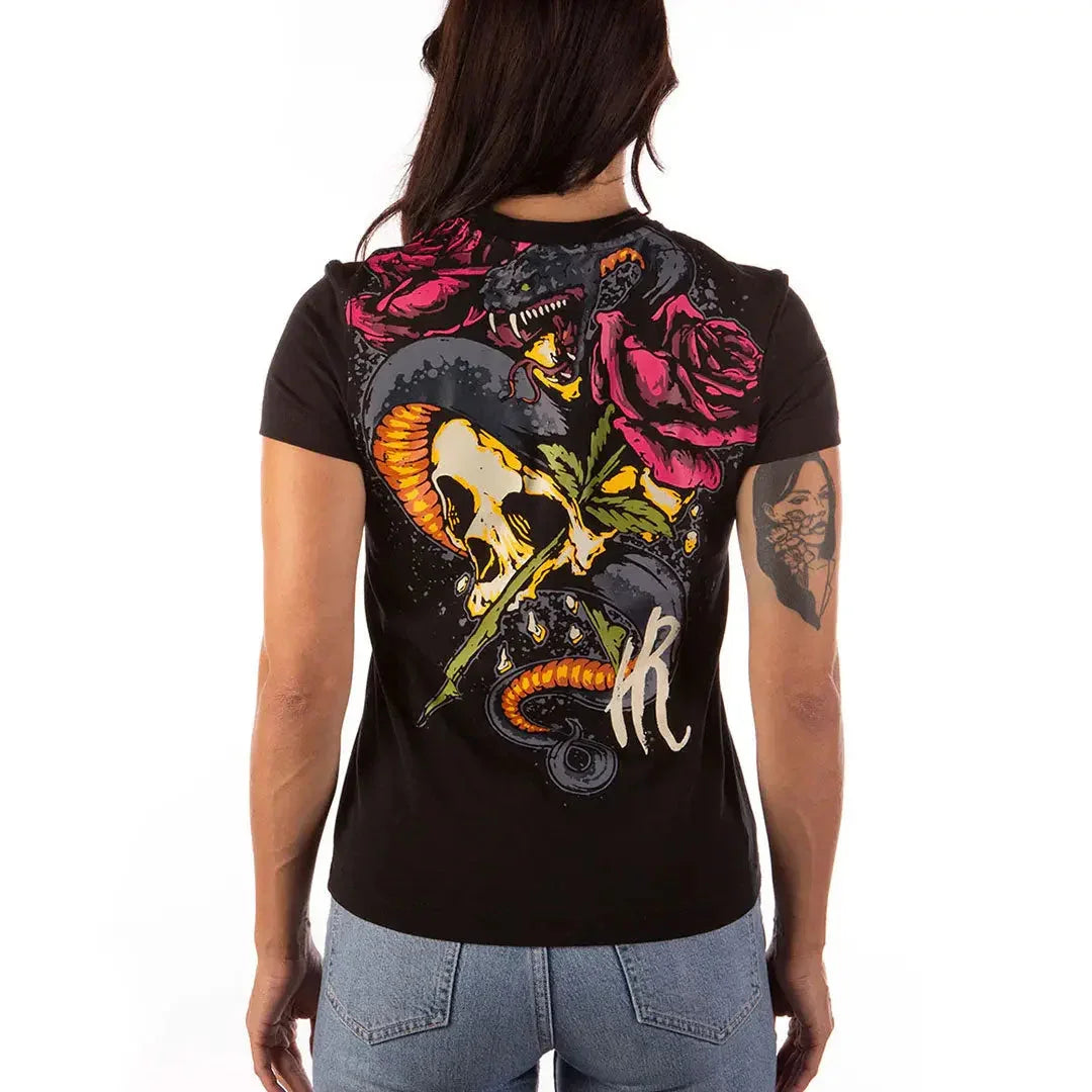 Woman wearing black shirt with skull, snake, rose graphic, tattoo on left arm, denim jeans
