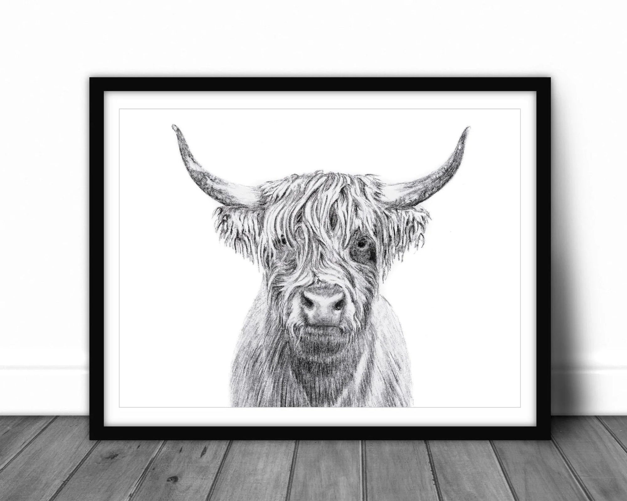 Framed black and white highland cow art print on wooden floor against white wall