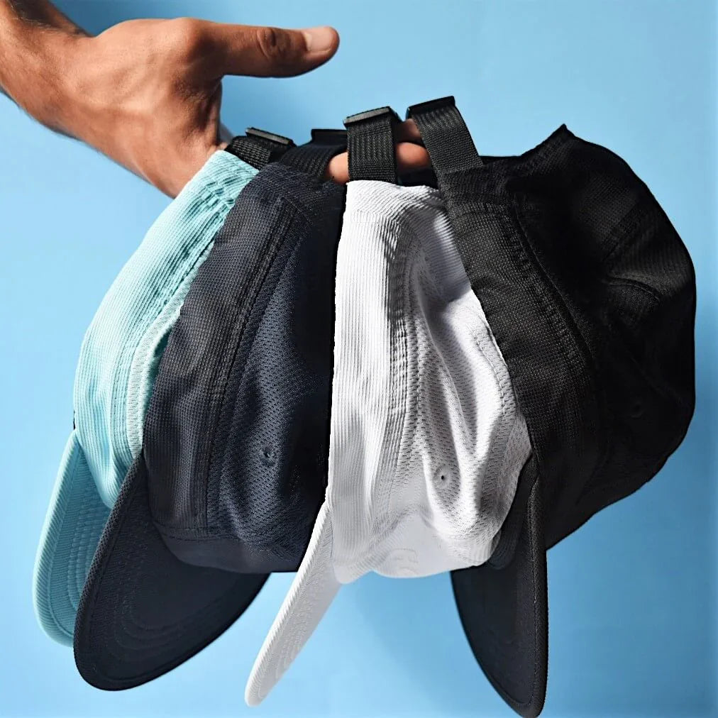 Hand holding four mesh baseball caps in blue, black, and white against a blue background
