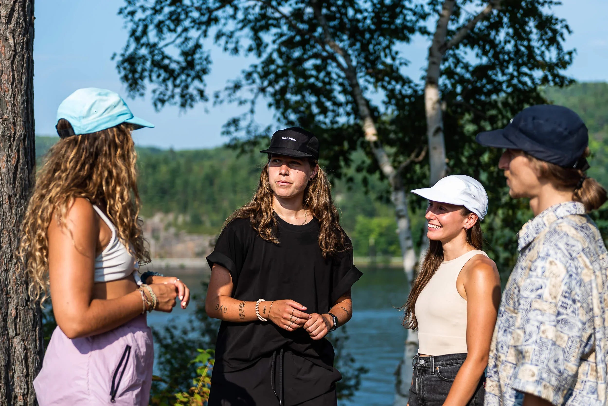 Group of young adults wearing lifestyle caps outdoors by a lake with trees in summer