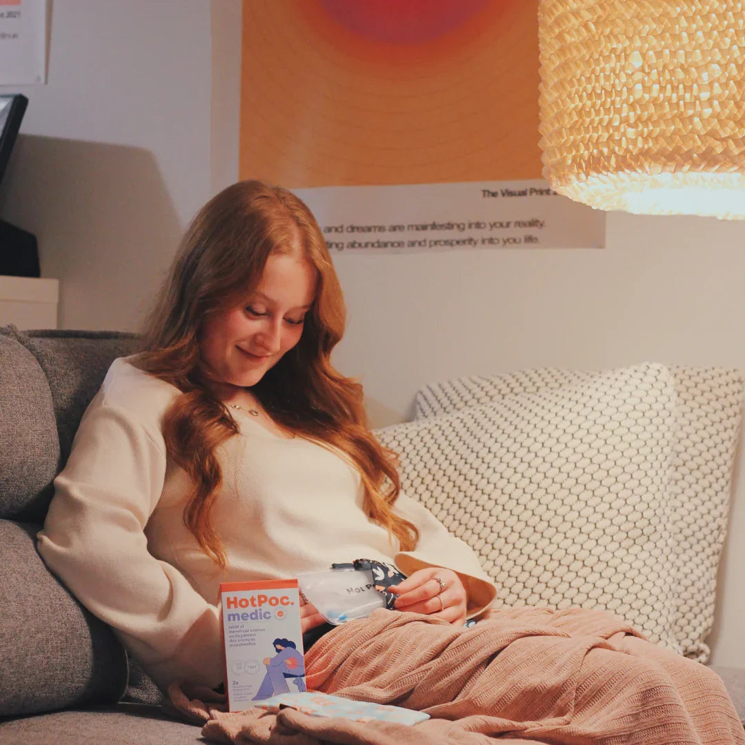 Woman relaxing on sofa using HotPoc medic heat pack, cozy home setting