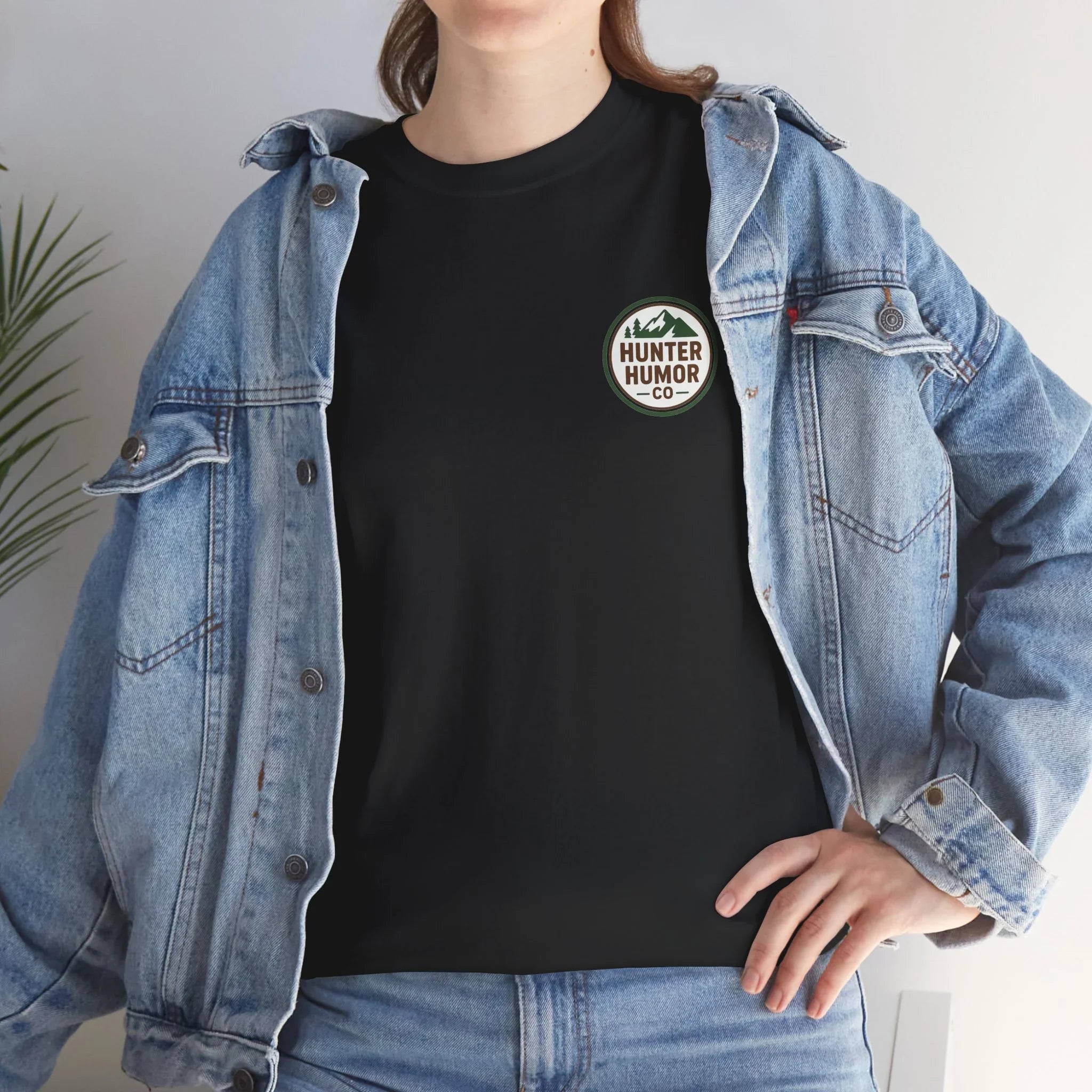 Person wearing black Hunter Humor Co t-shirt, denim jacket, and jeans indoors