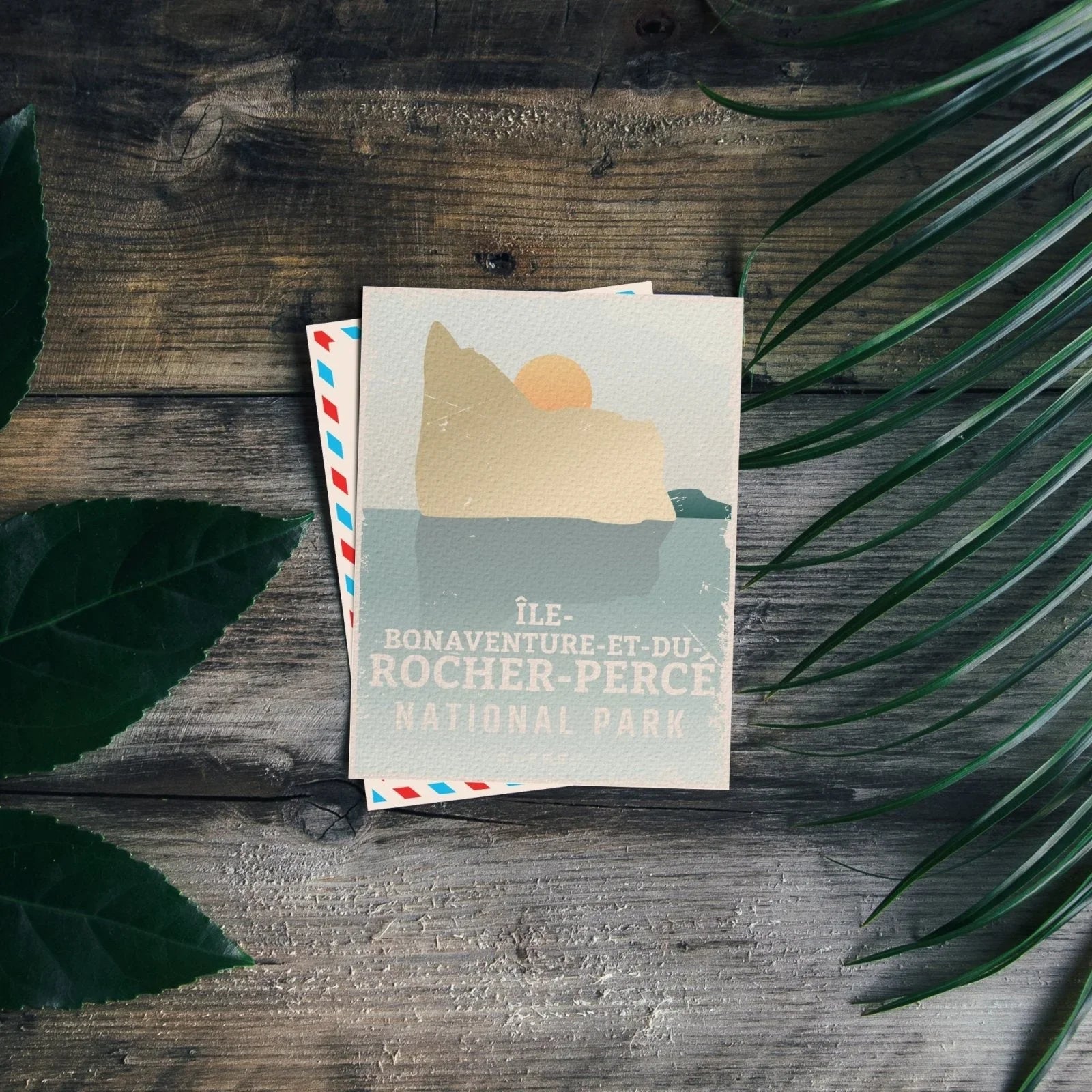 Ile Bonaventure et du Rocher Perce National Park postcard on wooden table with green leaves