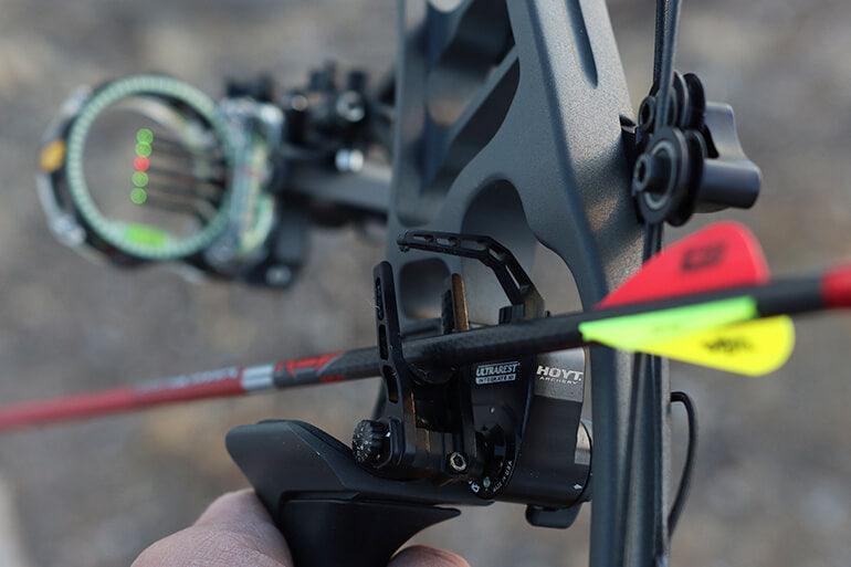 Compound bow close-up showing arrow rest installation and target sight outdoors