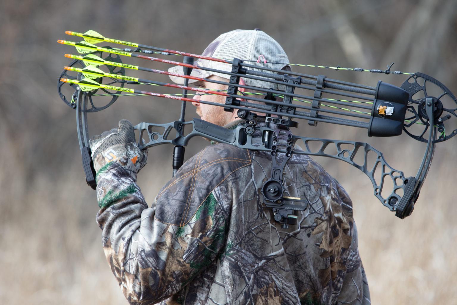 Hunter in camo jacket carrying compound bow with arrow quiver outdoors