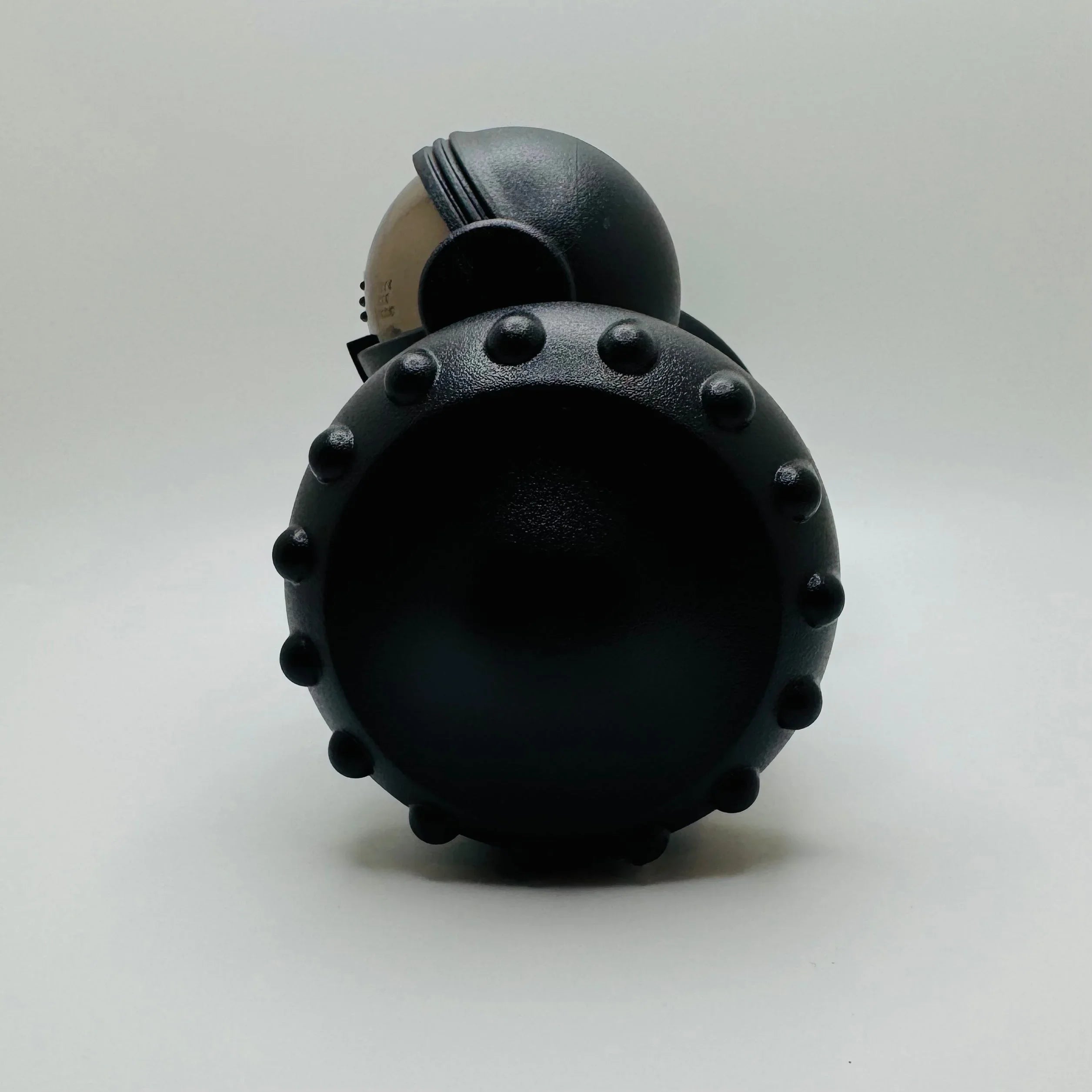 Black round toy with textured bumps and helmet on plain white background