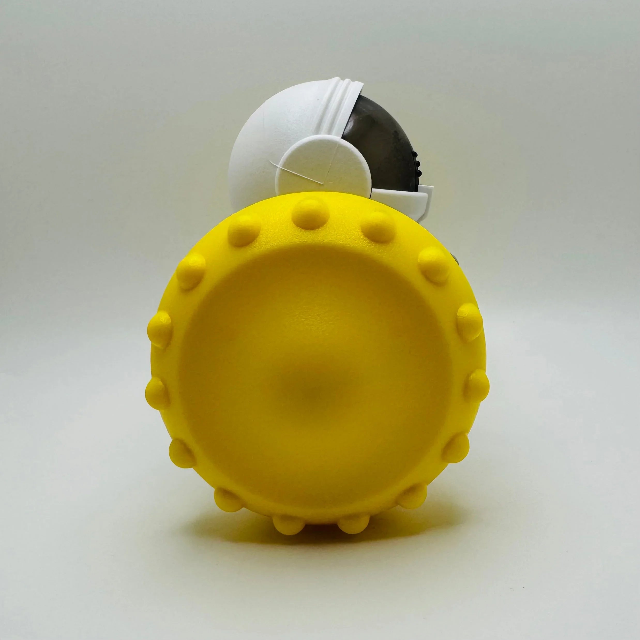 Yellow spiked pet toy with a white and black dome top on a plain background