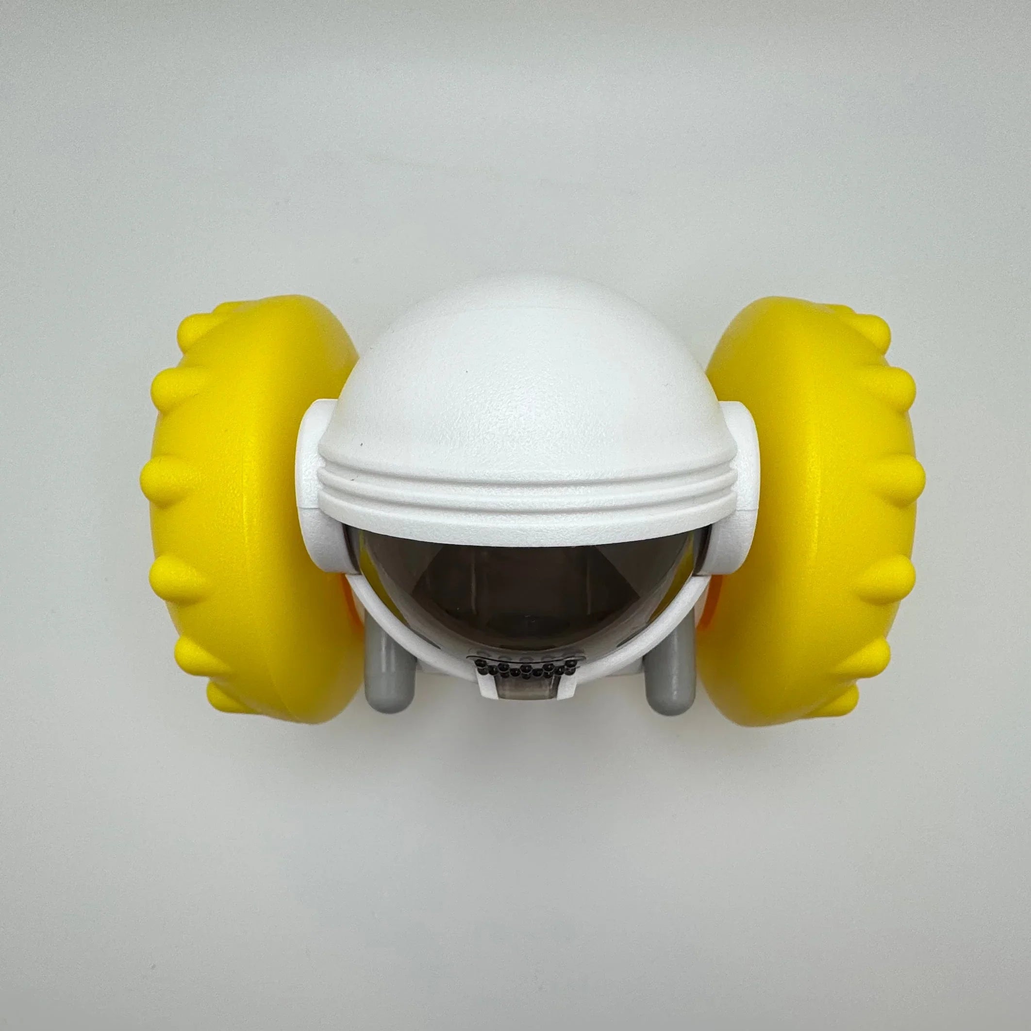 White and yellow astronaut-shaped dog toy with textured rubber wheels on a plain background