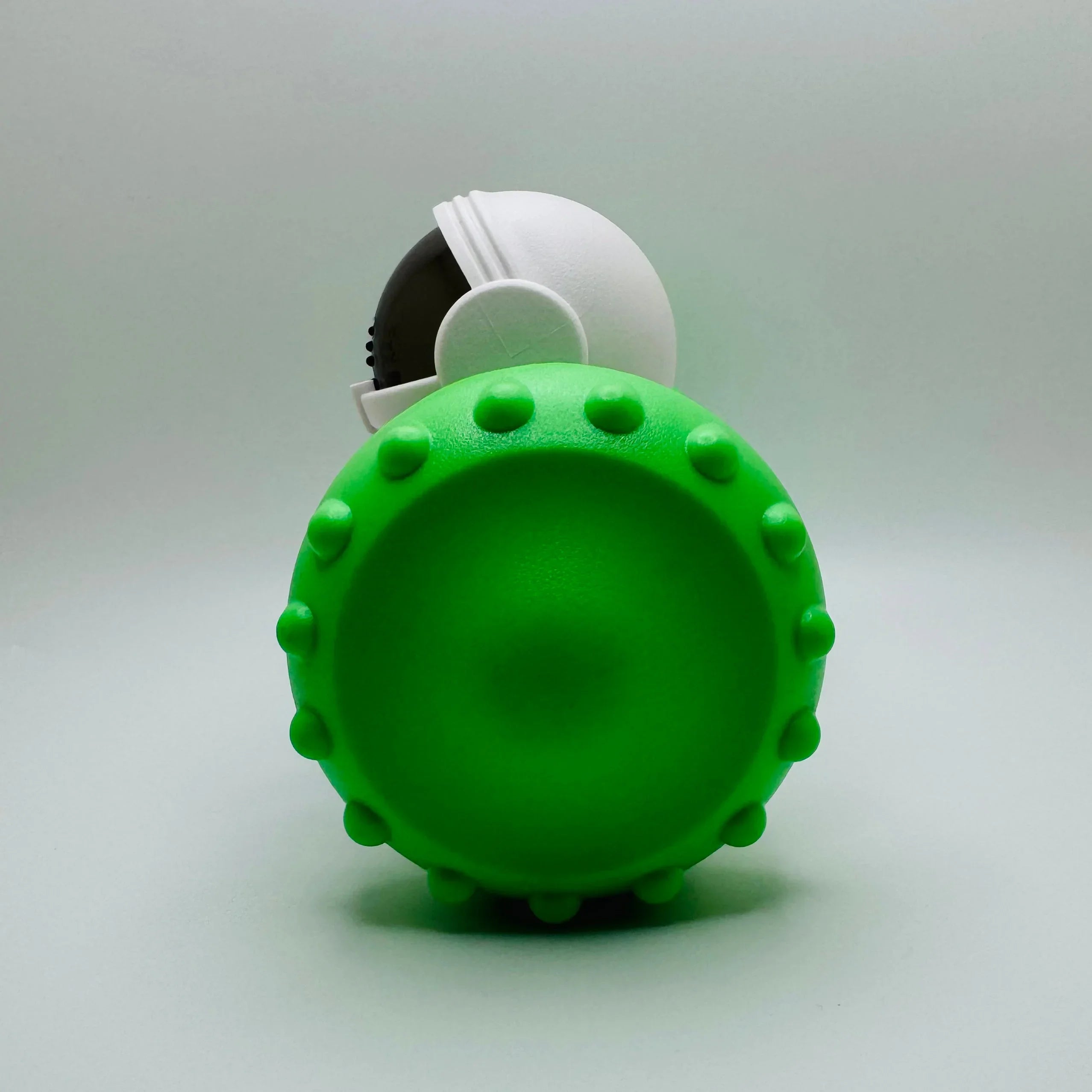 Green spiked rubber dog toy with astronaut figure on white background