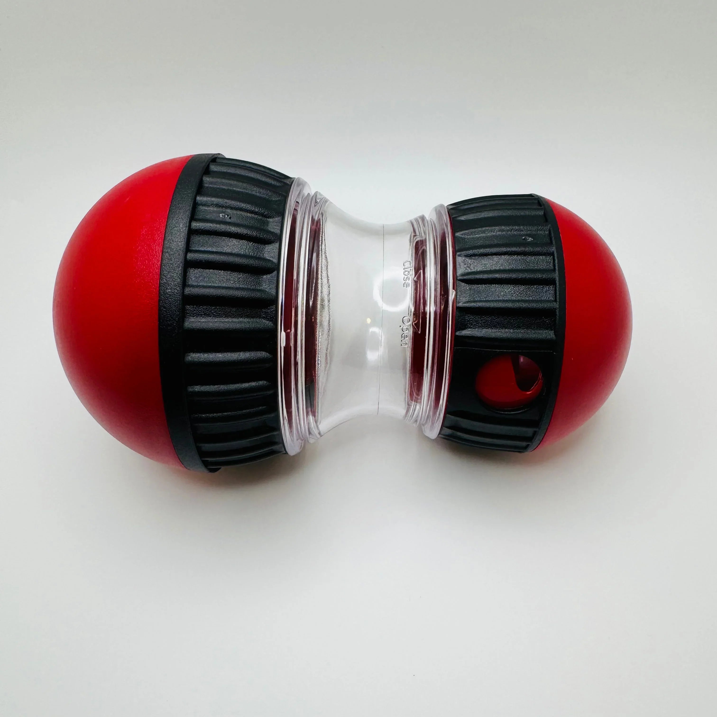 Red and black dog treat dispenser toy with clear center, pet enrichment product on white background.