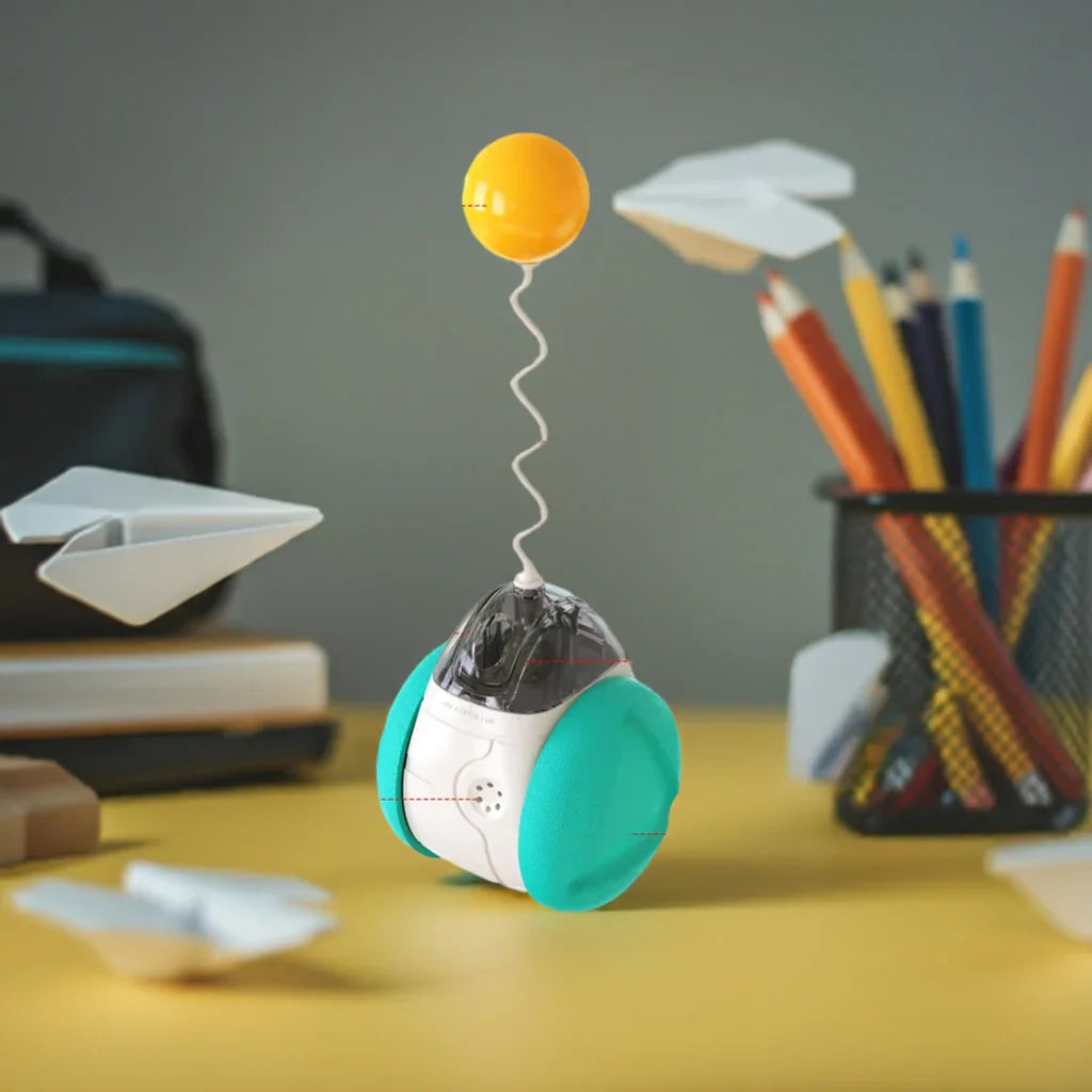 Cute robot toy with teal wheels and yellow antenna on a desk, surrounded by pencils and paper planes
