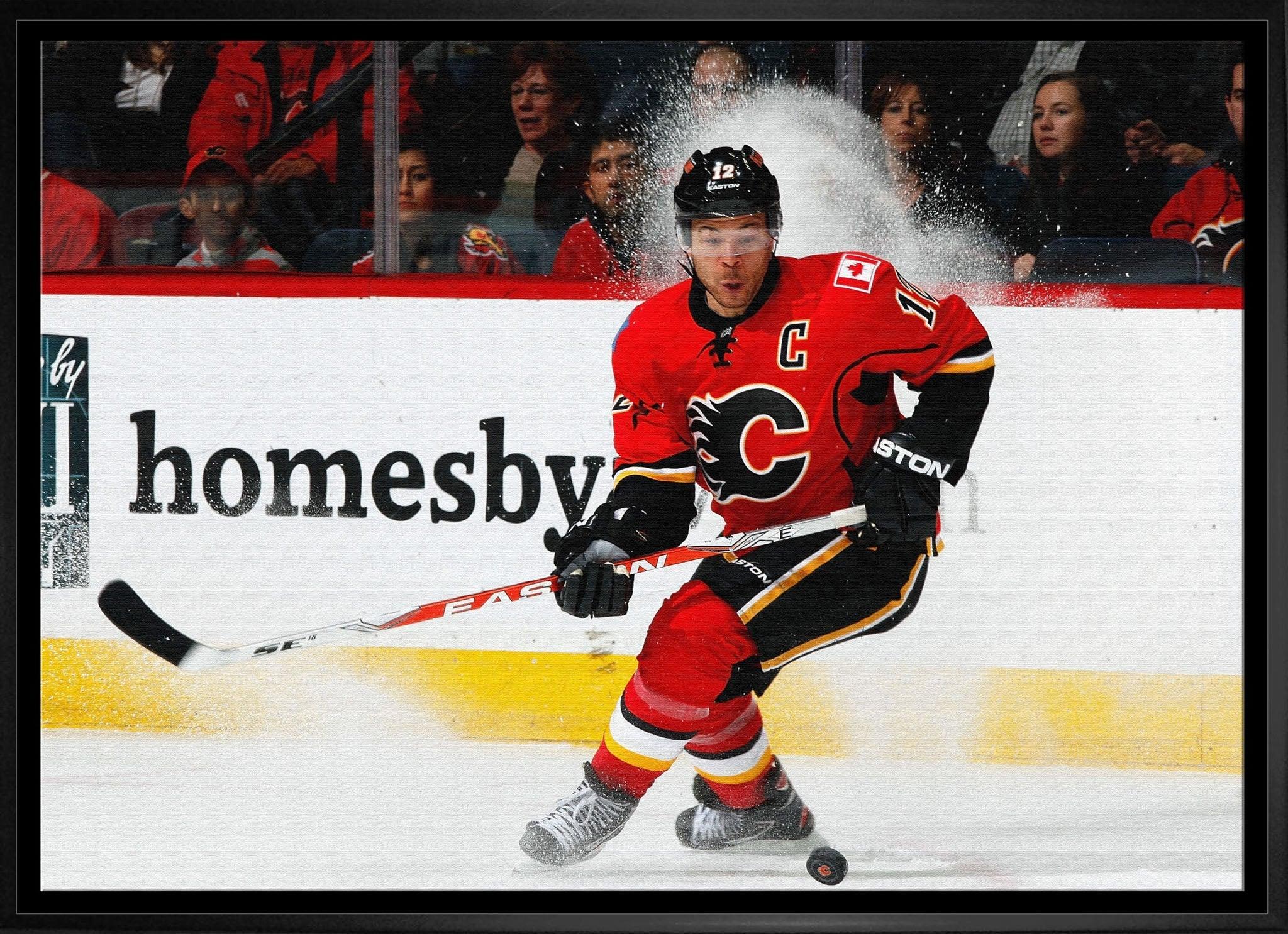 Calgary Flames hockey player in red jersey skating on ice during game, puck in motion