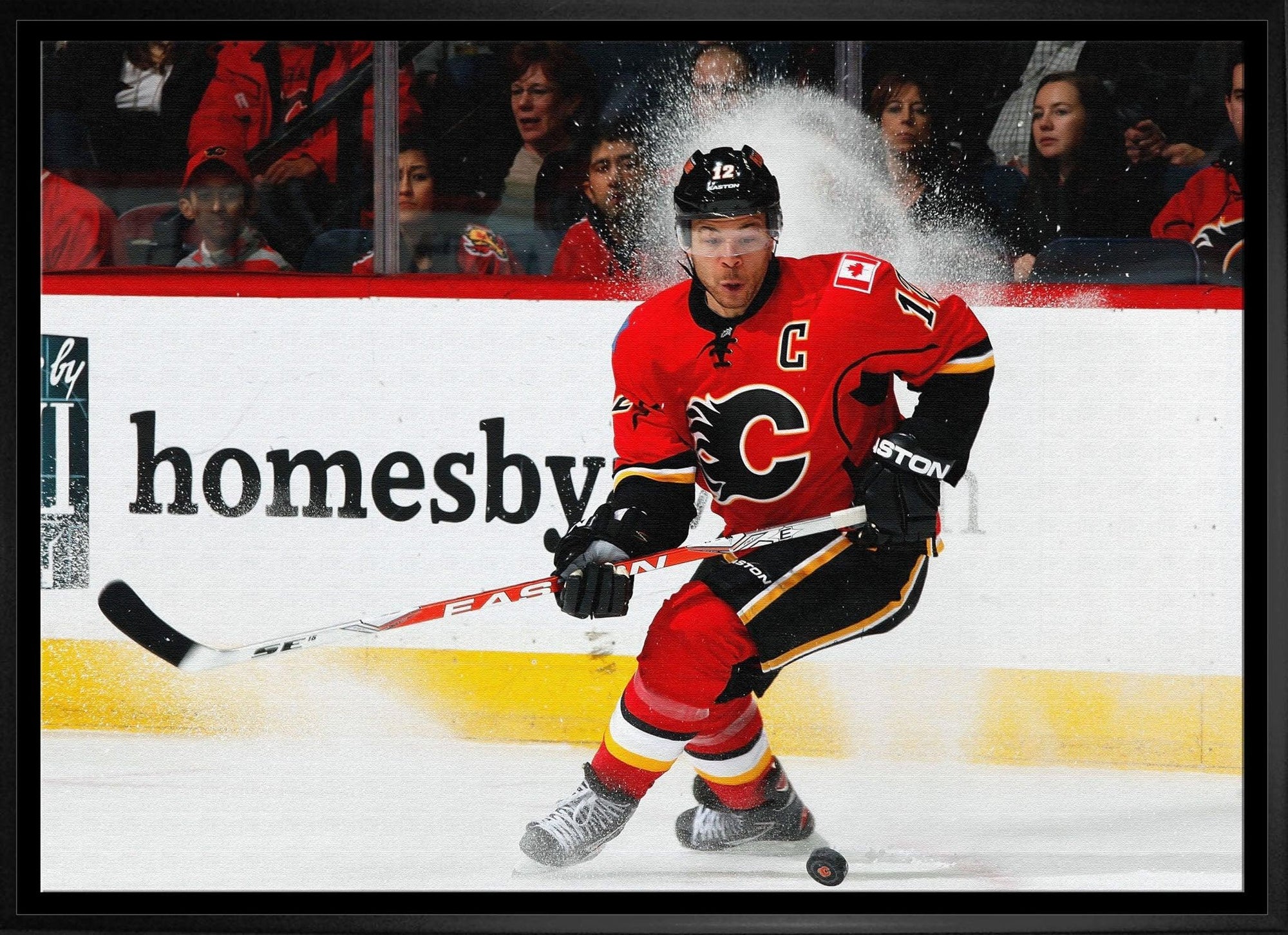 Calgary Flames hockey player in red jersey skating on ice during game, puck in motion